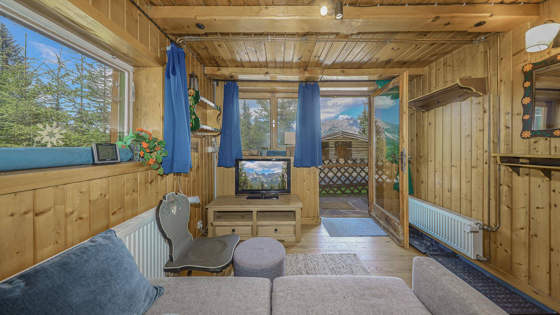 Heller Wohnbereich mit Sofa, Fernseher und direktem Zugang zu einem Außenbereich mit Bergblick.