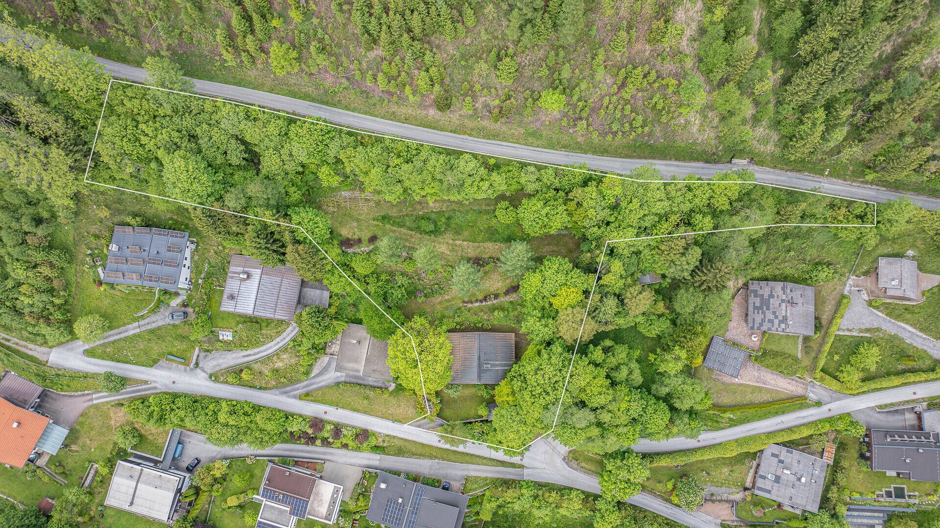 Luftaufnahme eines Grundstücks mit markierten Grenzen, umgeben von viel Grün und einer Straße.