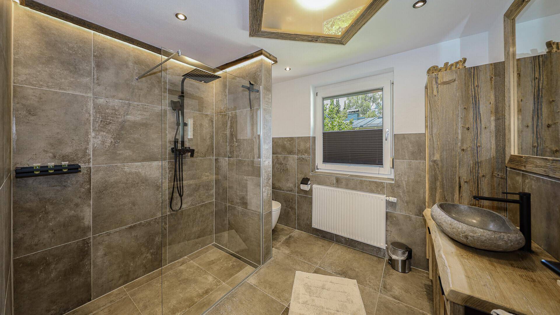 Modernes Badezimmer mit großformatigen Fliesen, begehbarer Dusche und einem Natursteinwaschbecken.