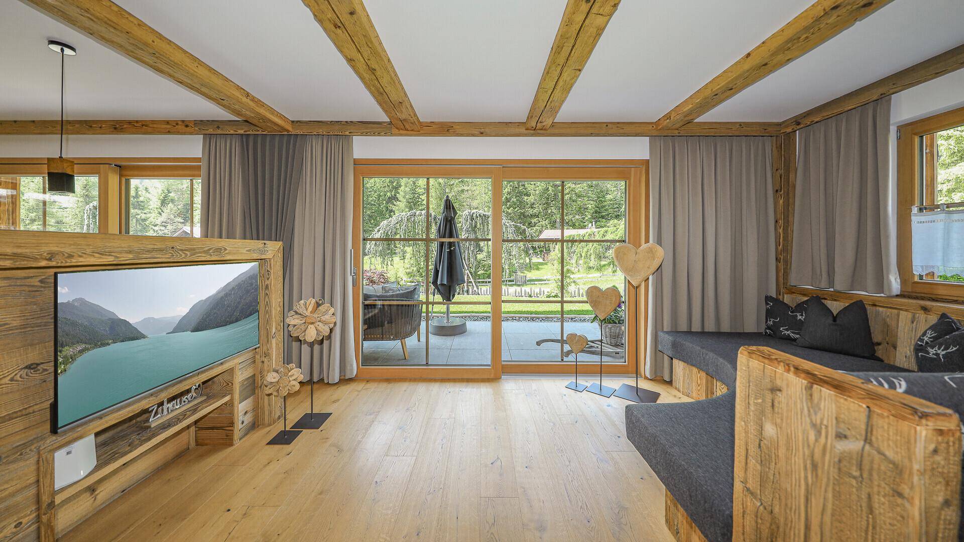 Heller Wohnbereich mit Holzbalkendecke, großen Schiebetüren zur Terrasse und gemütlicher Sitzecke.