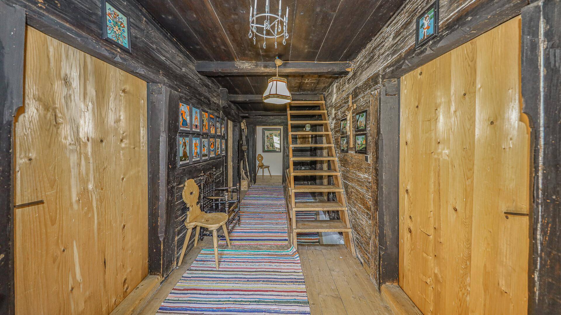 Rustikaler Flur mit dunklen Holzwänden, Holzboden und einer einfachen Holztreppe.