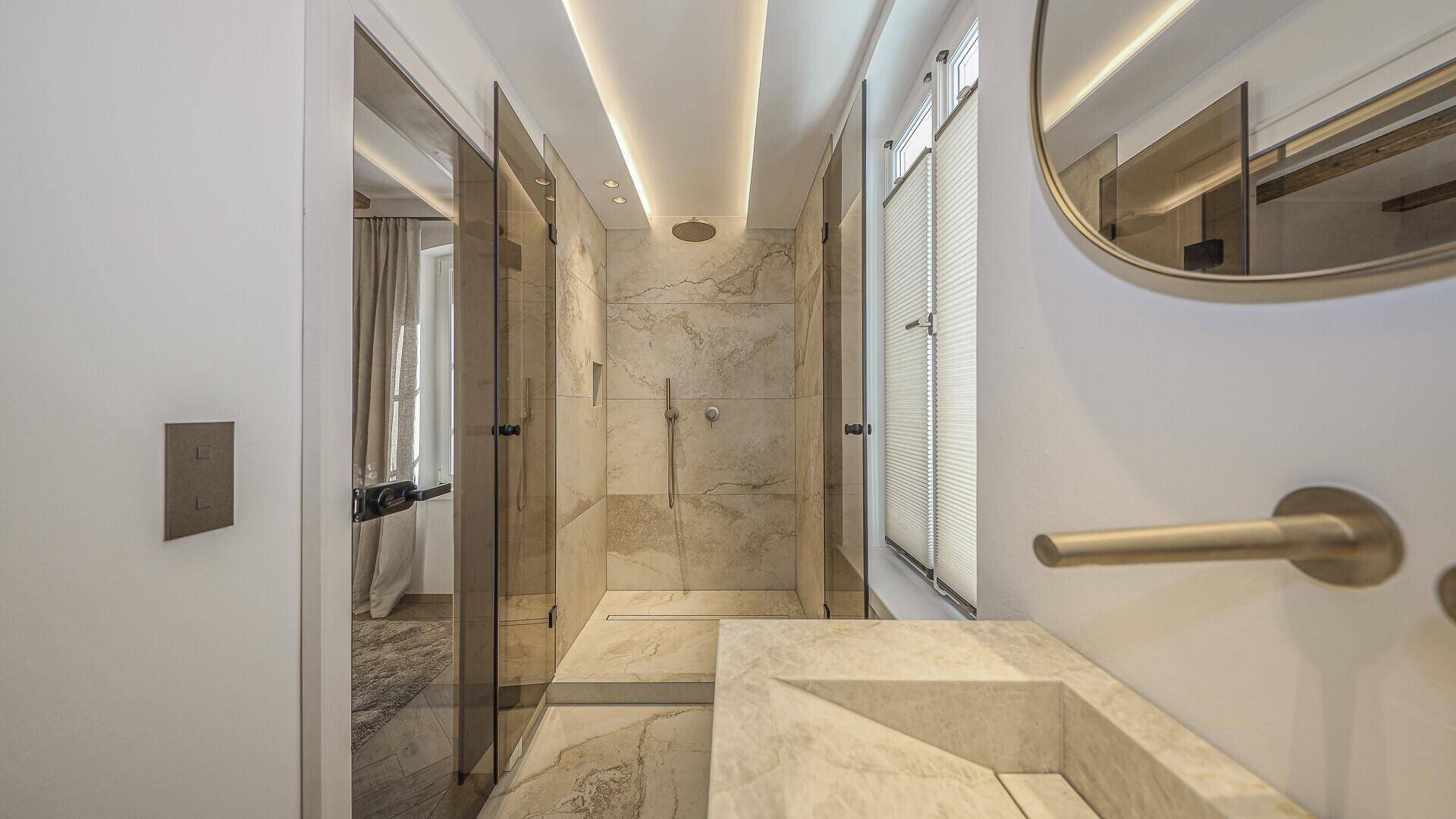 Elegantes Badezimmer mit großer begehbarer Dusche, Marmorfliesen und indirekter Beleuchtung.