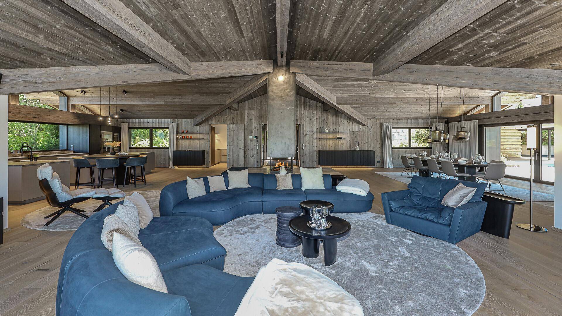 Gemütliches Wohnzimmer mit großer blauer Sofalandschaft, Holzbalkendecke und modernem Kamin.