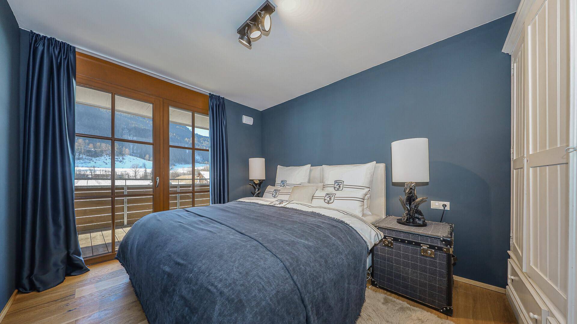 Schlafzimmer mit blau gestrichenen Wänden, Holzboden und direktem Zugang zu einem Balkon mit Bergblick.