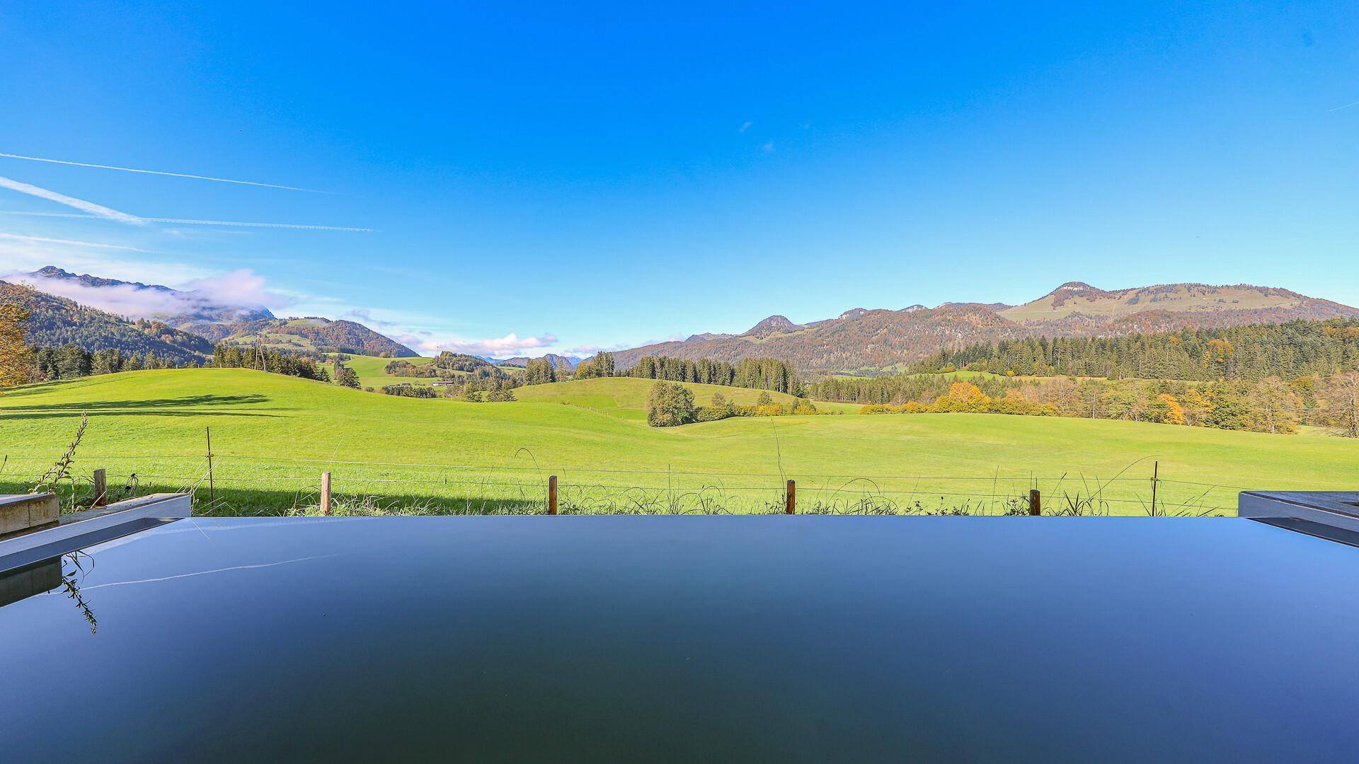 Ruhiger Poolbereich mit unverbautem Blick auf die weite grüne Landschaft und die Berge.