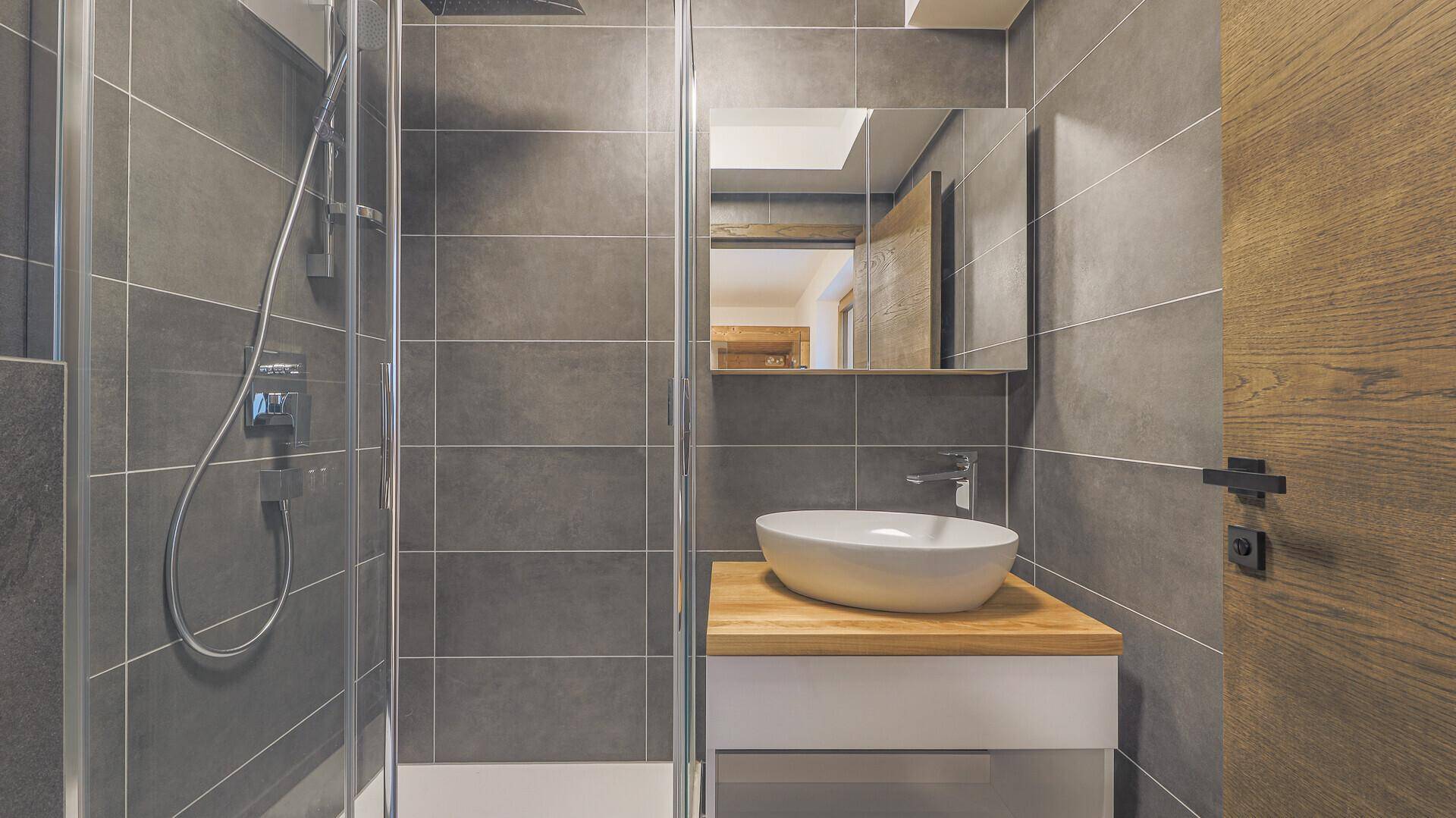 Kleines Badezimmer mit Dusche, Waschbecken und Spiegel, ausgestattet mit grauen Fliesen.