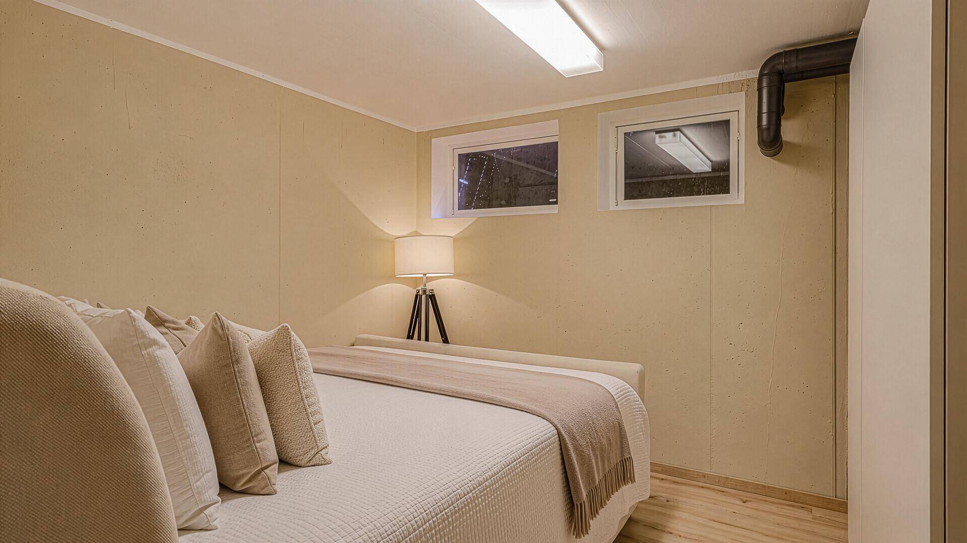 Gemütliches Schlafzimmer im Untergeschoss mit kleinem Fenster und heller Einrichtung.