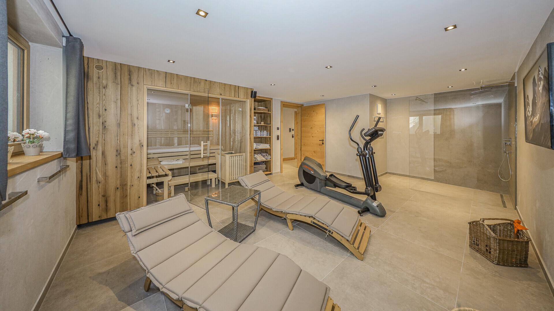 Wellnessbereich mit Sauna, Liegen und Fitnessgerät für Entspannung und Sport.