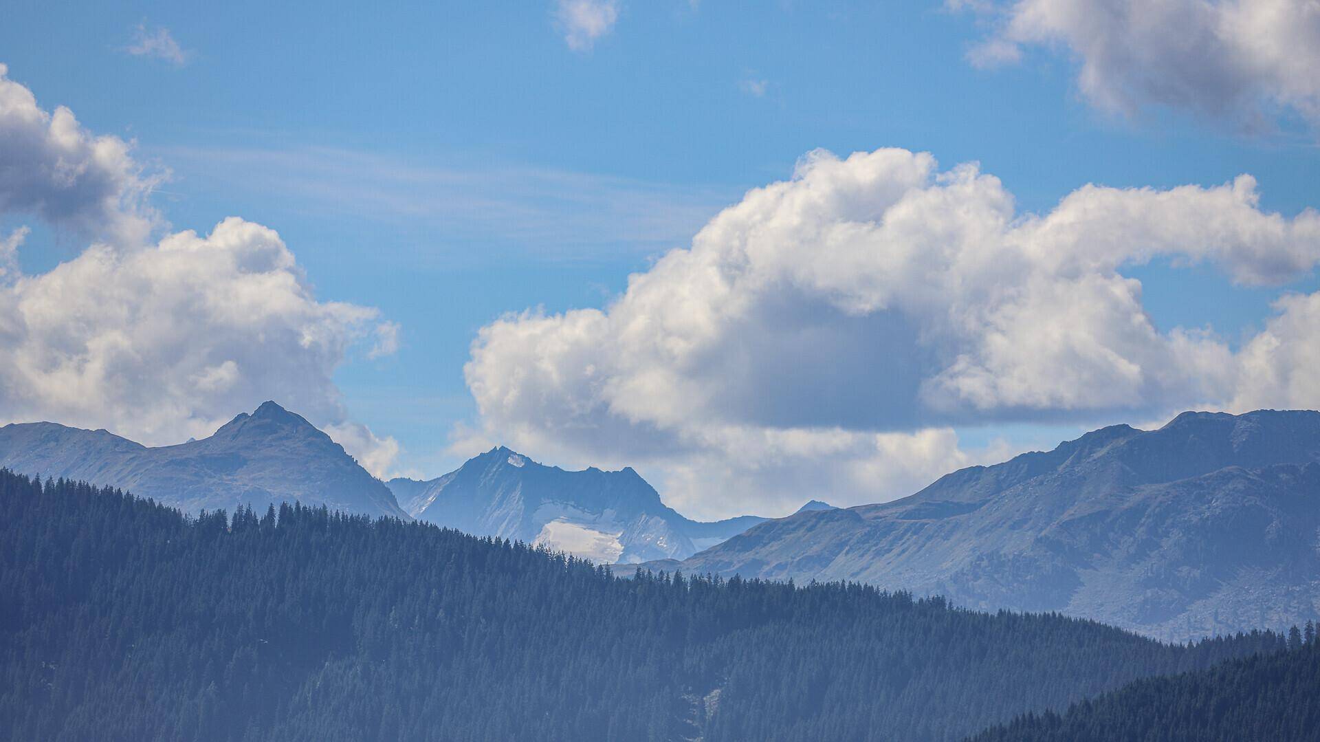 Majestätische Berglandschaft mit bewaldeten Hängen und weiten Tälern unter blauem Himmel.