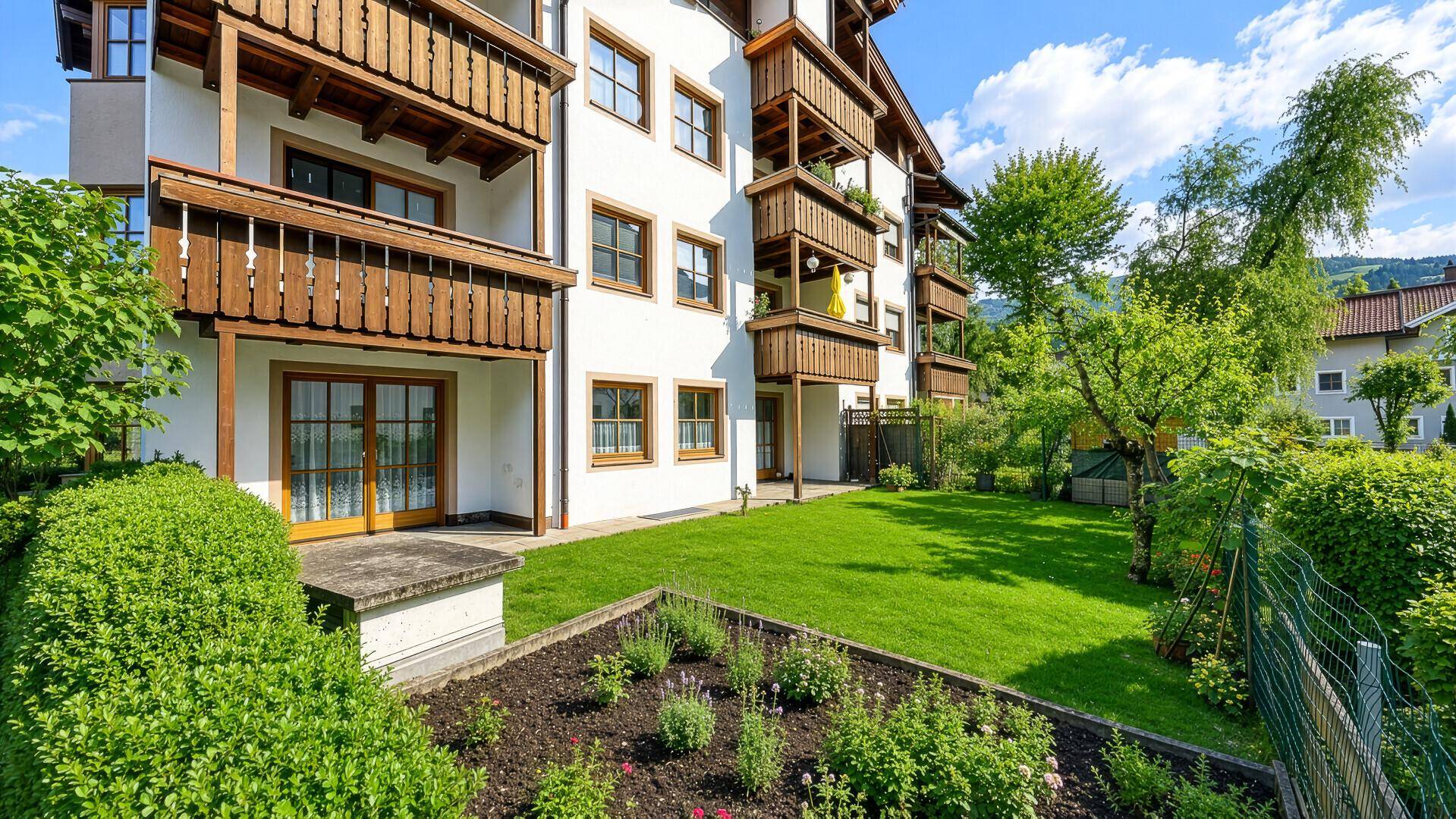 Hausfassade mit Balkonen und gepflegtem Gartenbereich mit Blumenbeeten.