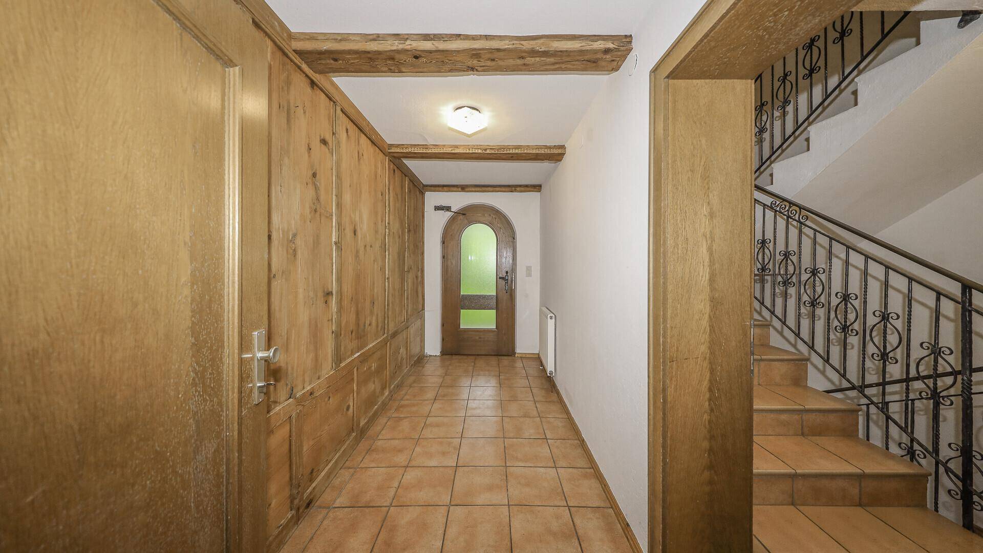 Traditioneller Flur mit Holzvertäfelung, Fliesenboden und schmiedeeiserner Treppe.