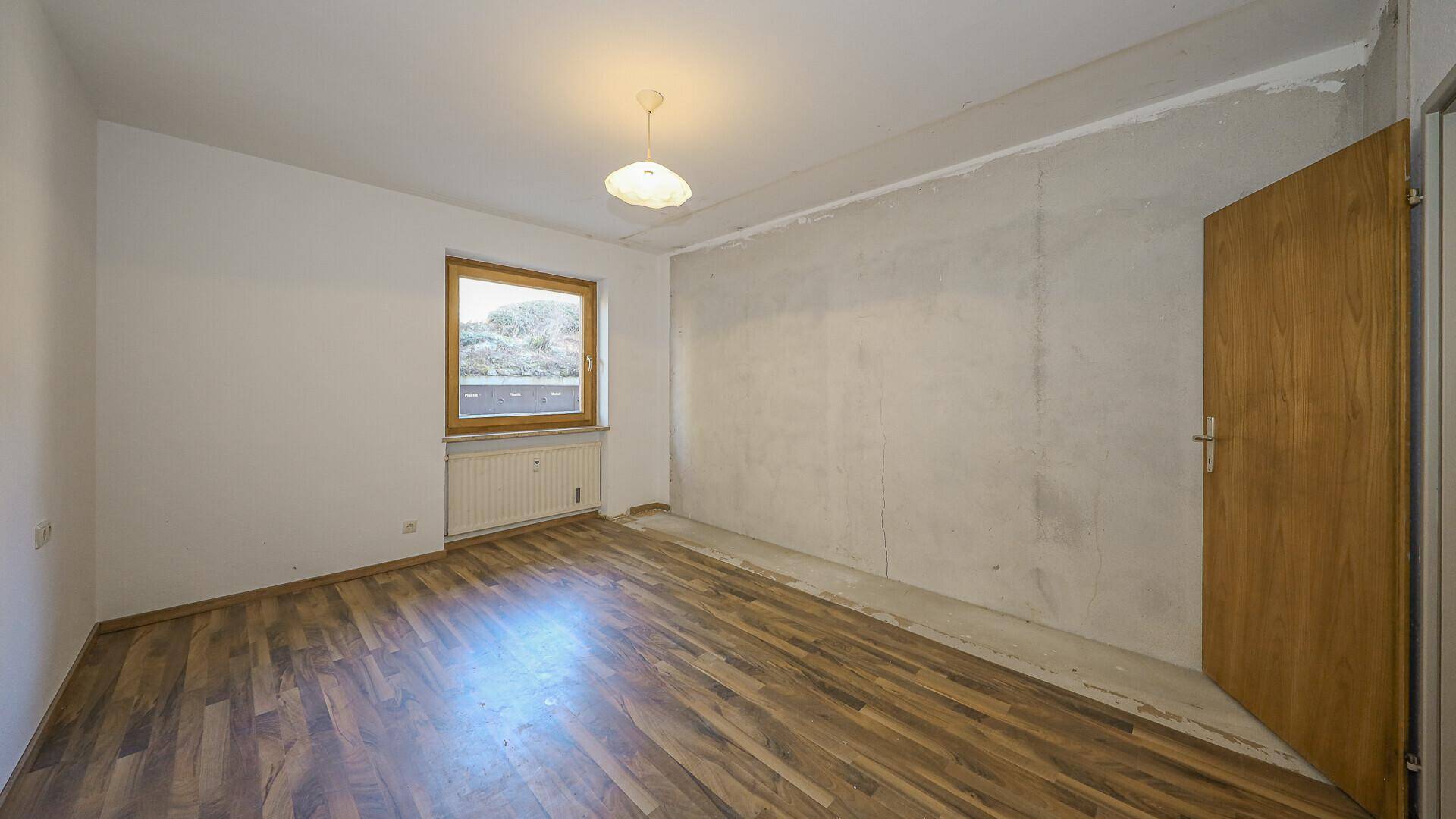 Leeres Schlafzimmer mit Holzboden, weiß gestrichenen Wänden und einer Sichtbetonwand.
