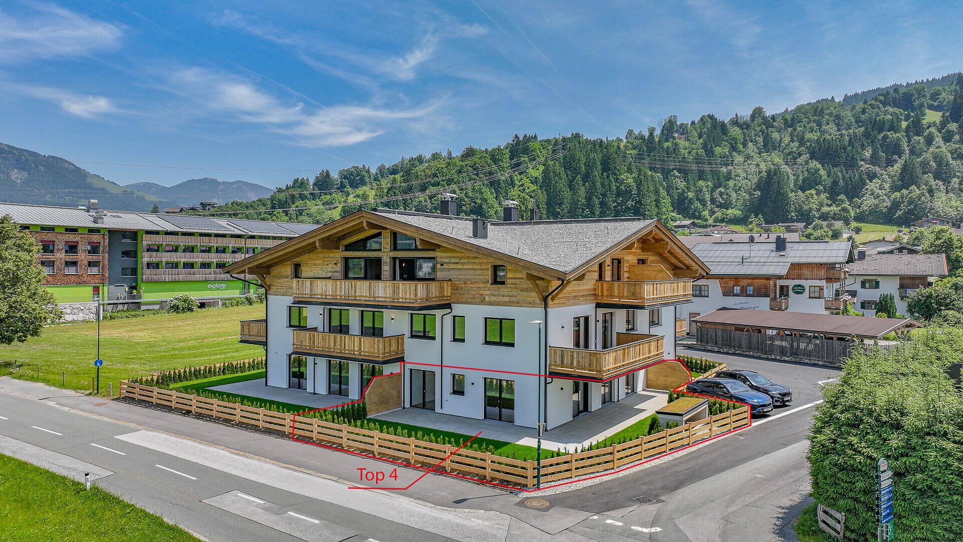 Moderne Wohnanlage mit Holzfassade, Balkonen und umzäunten Gartenbereichen in alpiner Umgebung.