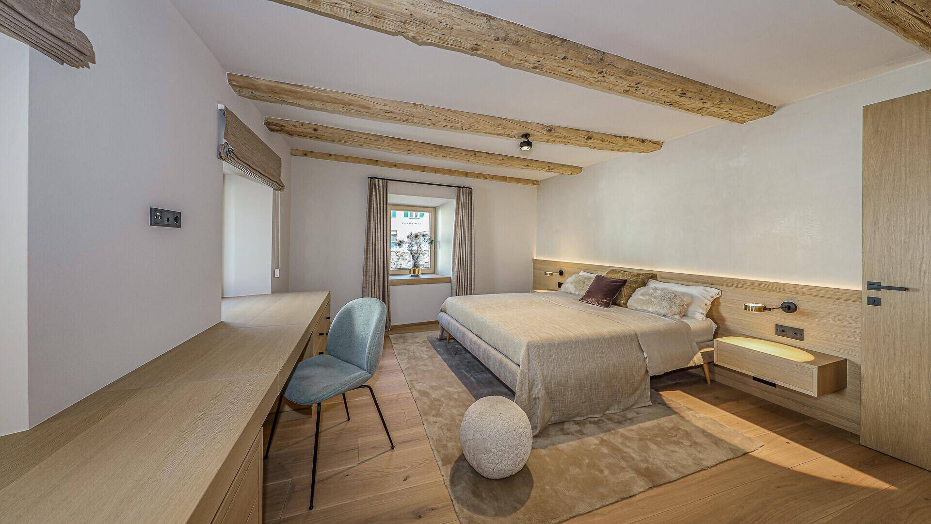 Gemütliches Schlafzimmer mit Holzbalken, Holzboden und integriertem Schreibtischbereich.