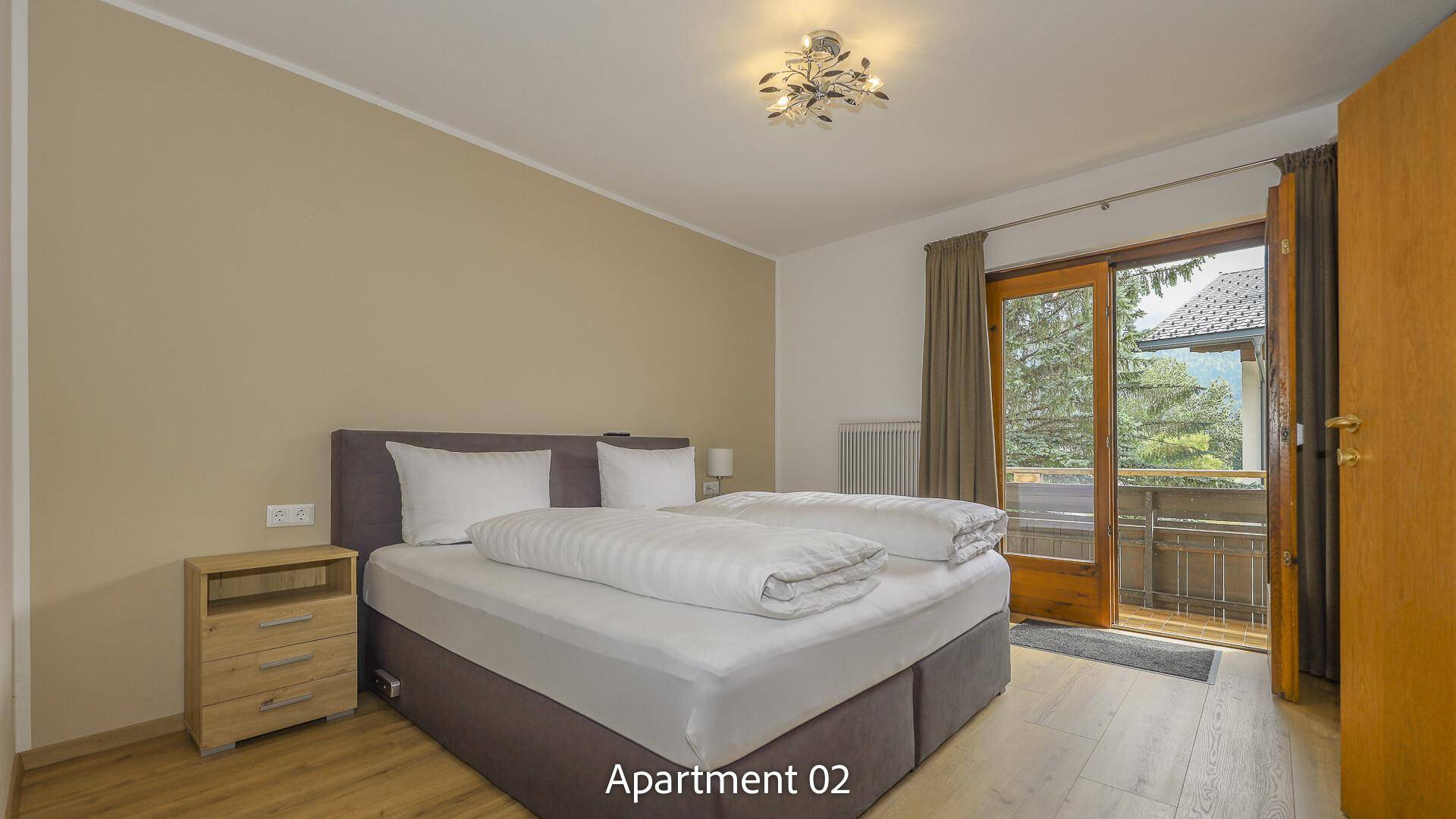 Helles Schlafzimmer von Apartment 02 mit Doppelbett, Nachttisch und direktem Zugang zum Balkon.