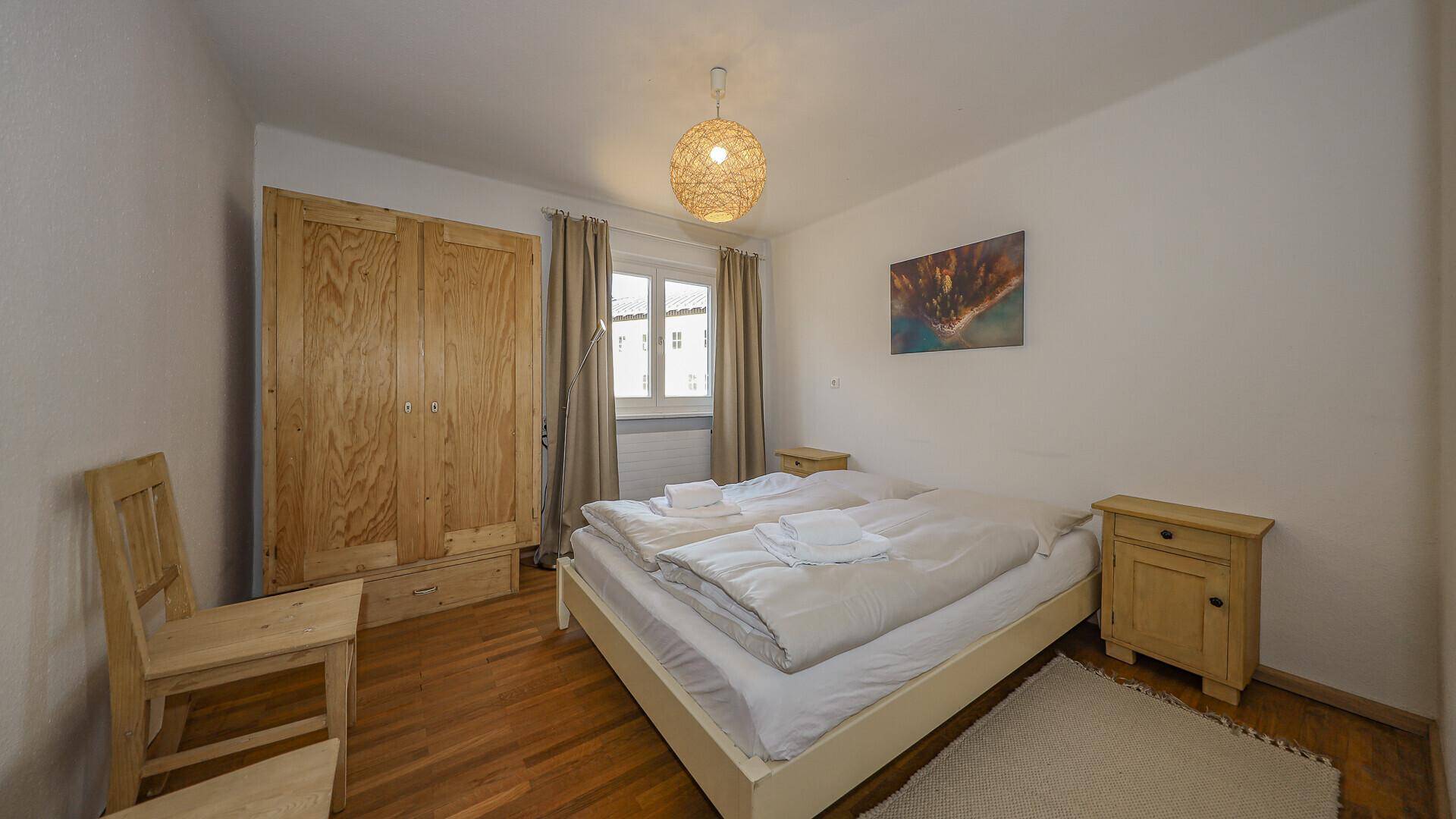 Helles Schlafzimmer mit Doppelbett, Holzschrank und Holzboden.