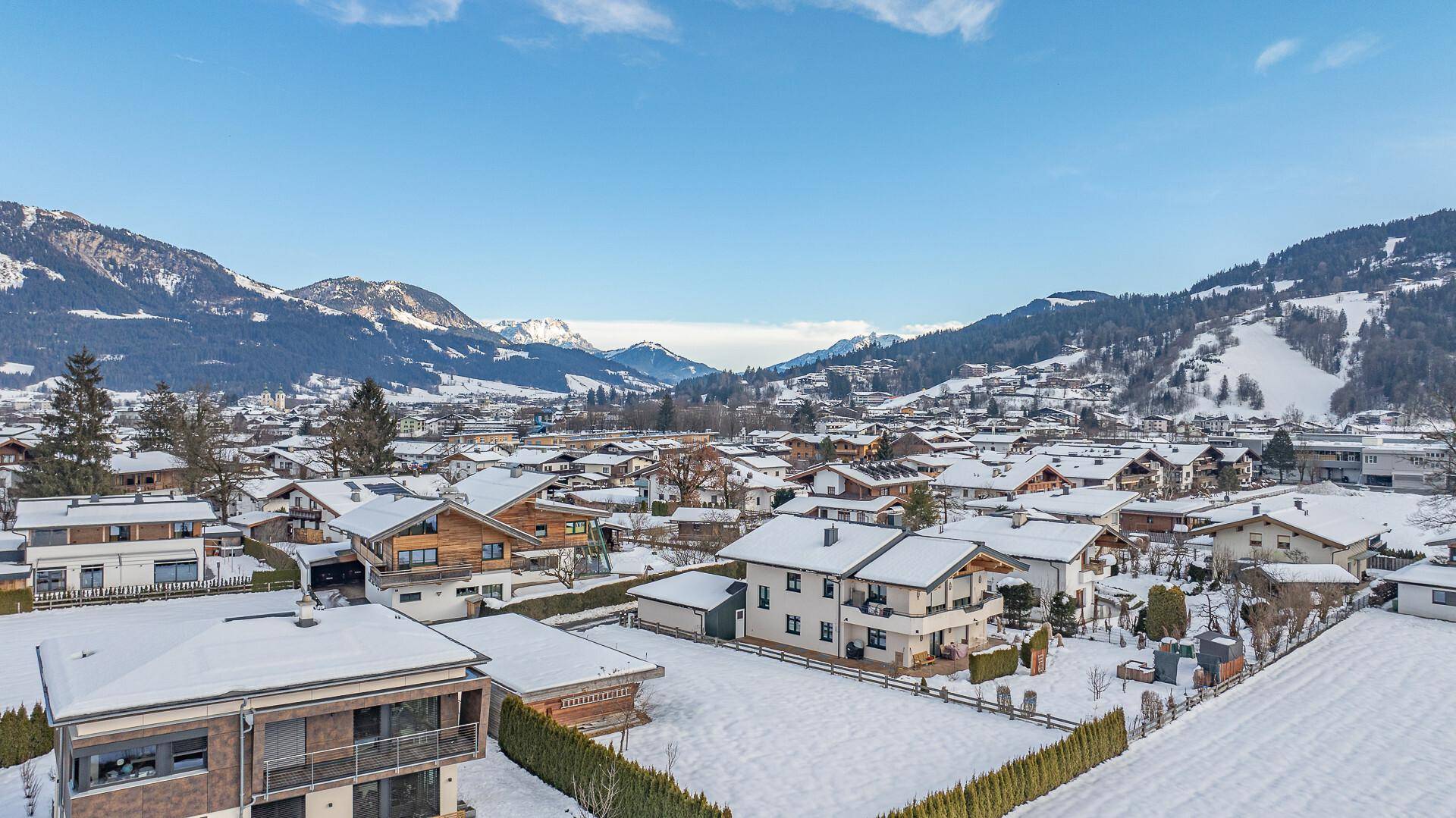 Weitläufige Luftaufnahme einer Siedlung in den Bergen mit verschneiten Dächern und Tälern.