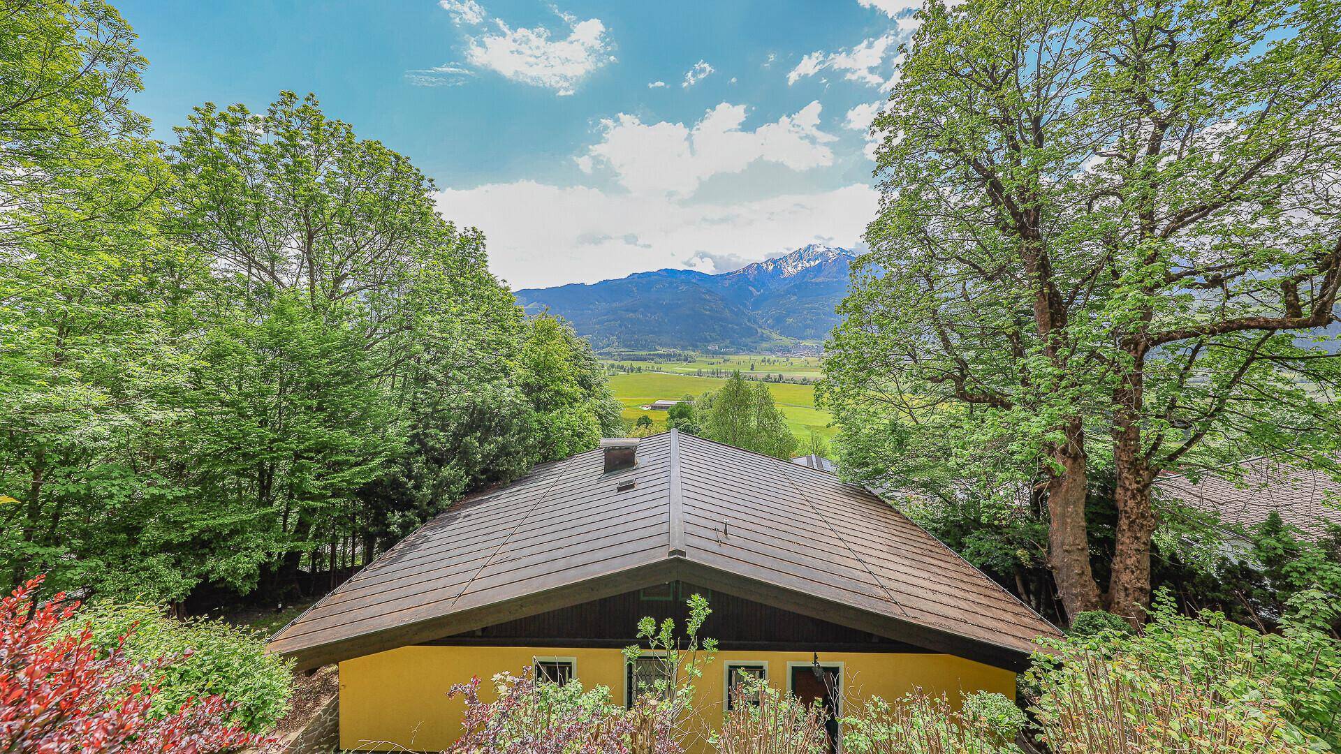 Dachansicht des gelben Hauses, umgeben von Bäumen, mit Bergblick im Hintergrund.