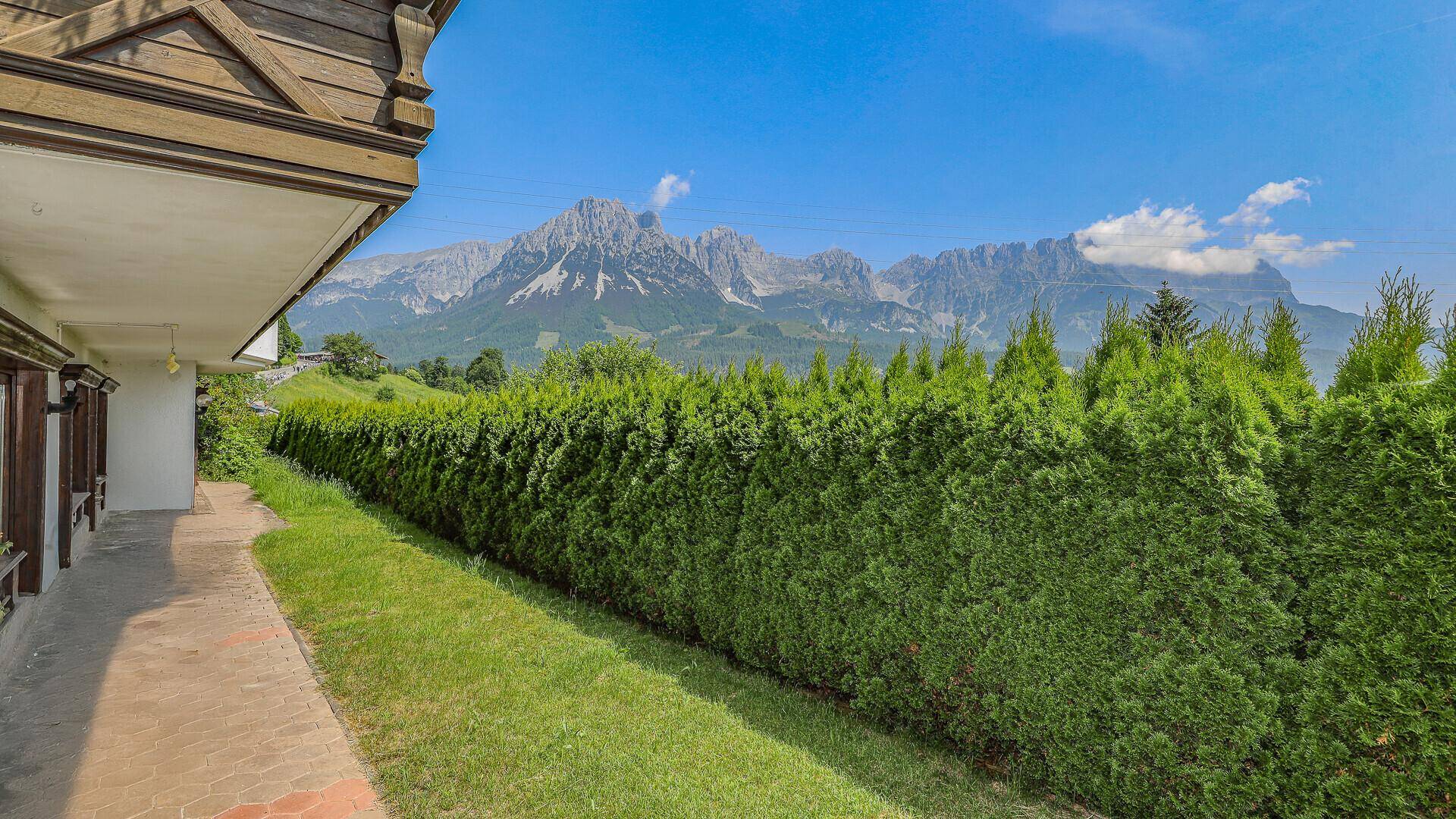 Gepflegter Gartenweg entlang einer hohen Hecke mit Blick auf die grüne Umgebung.