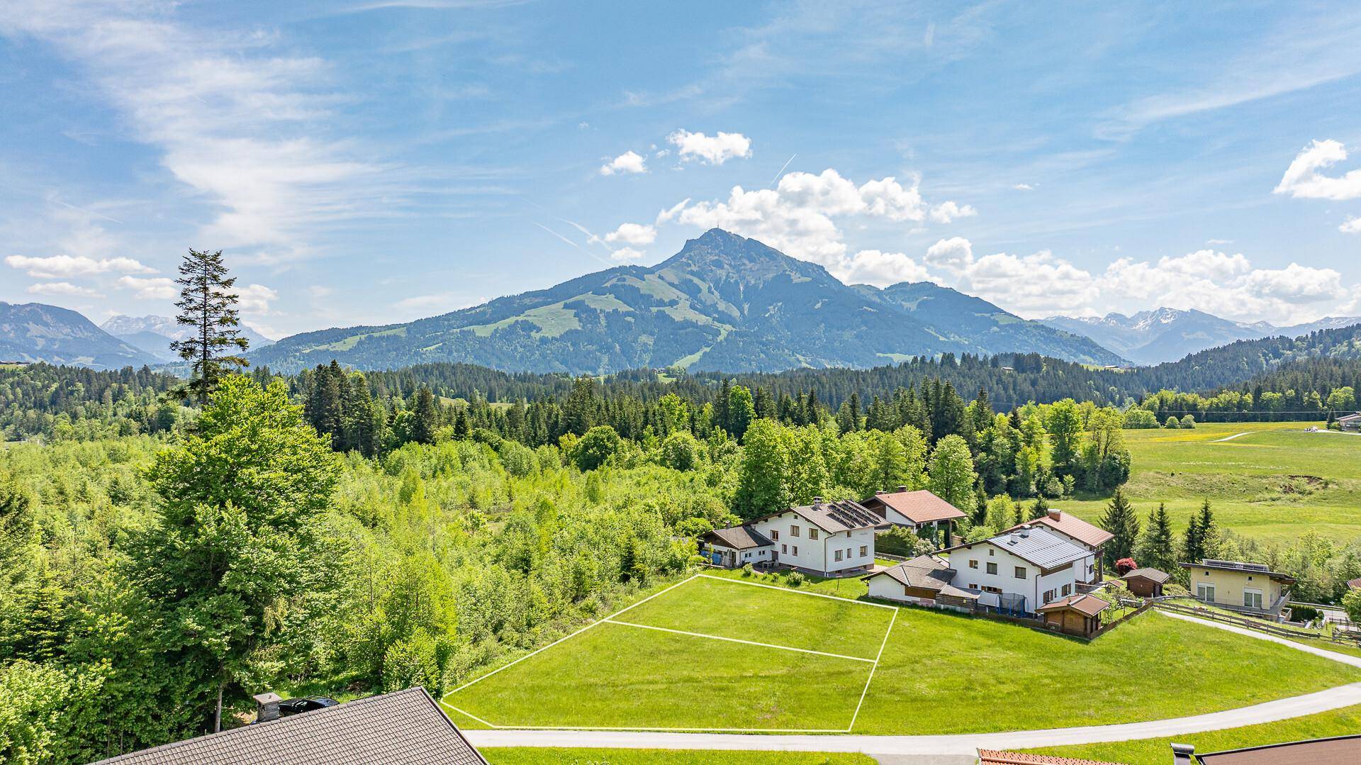 Idyllische Landschaft mit grünen Wiesen, Wäldern und einem freien Grundstück, umgeben von Häusern.