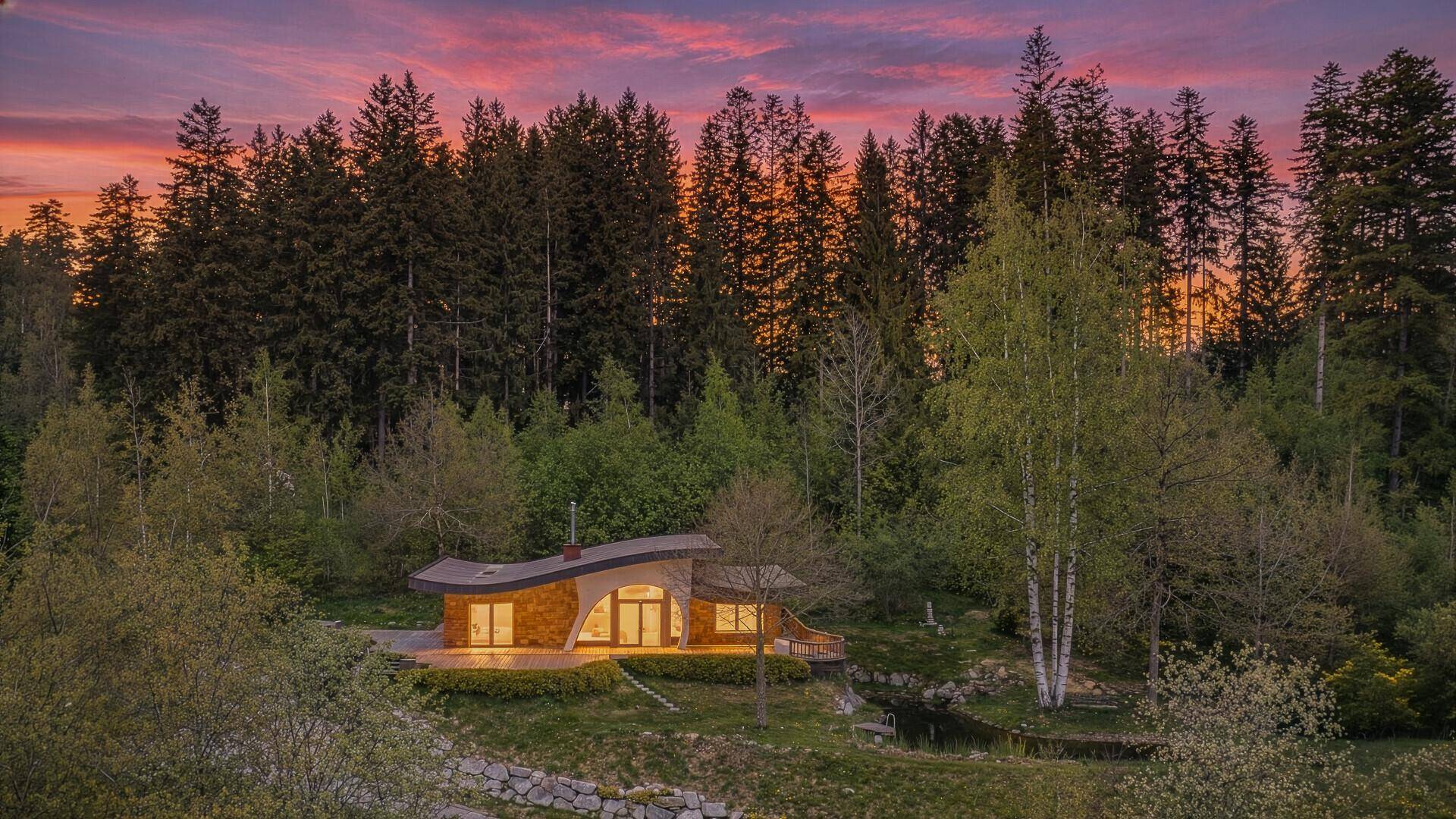 Panoramablick auf das moderne Haus bei Sonnenuntergang, eingebettet in die Waldlandschaft mit Teich.
