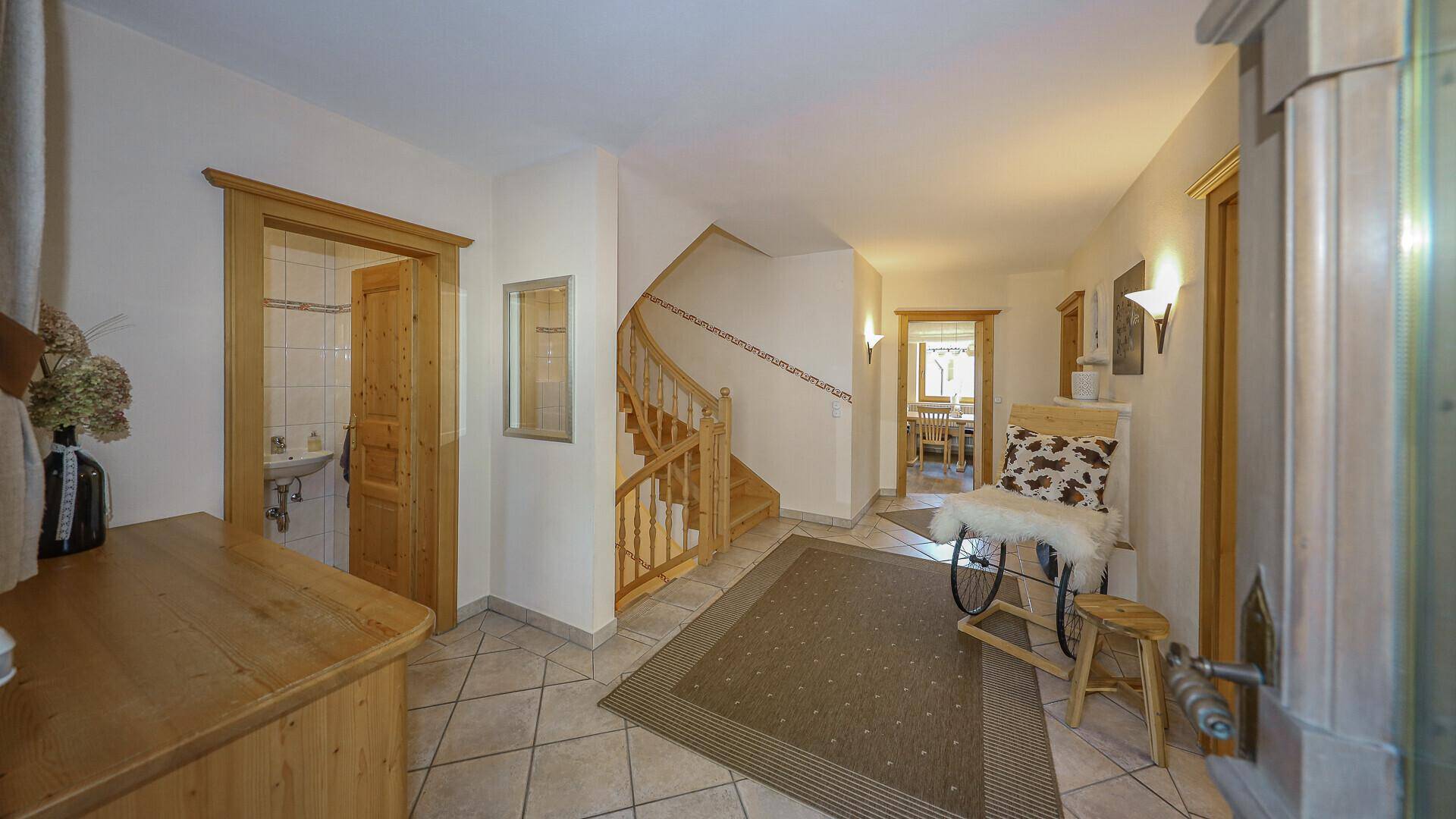 Heller Flur mit rustikalen Holztreppen, Fliesenboden und Zugang zu einem Badezimmer.