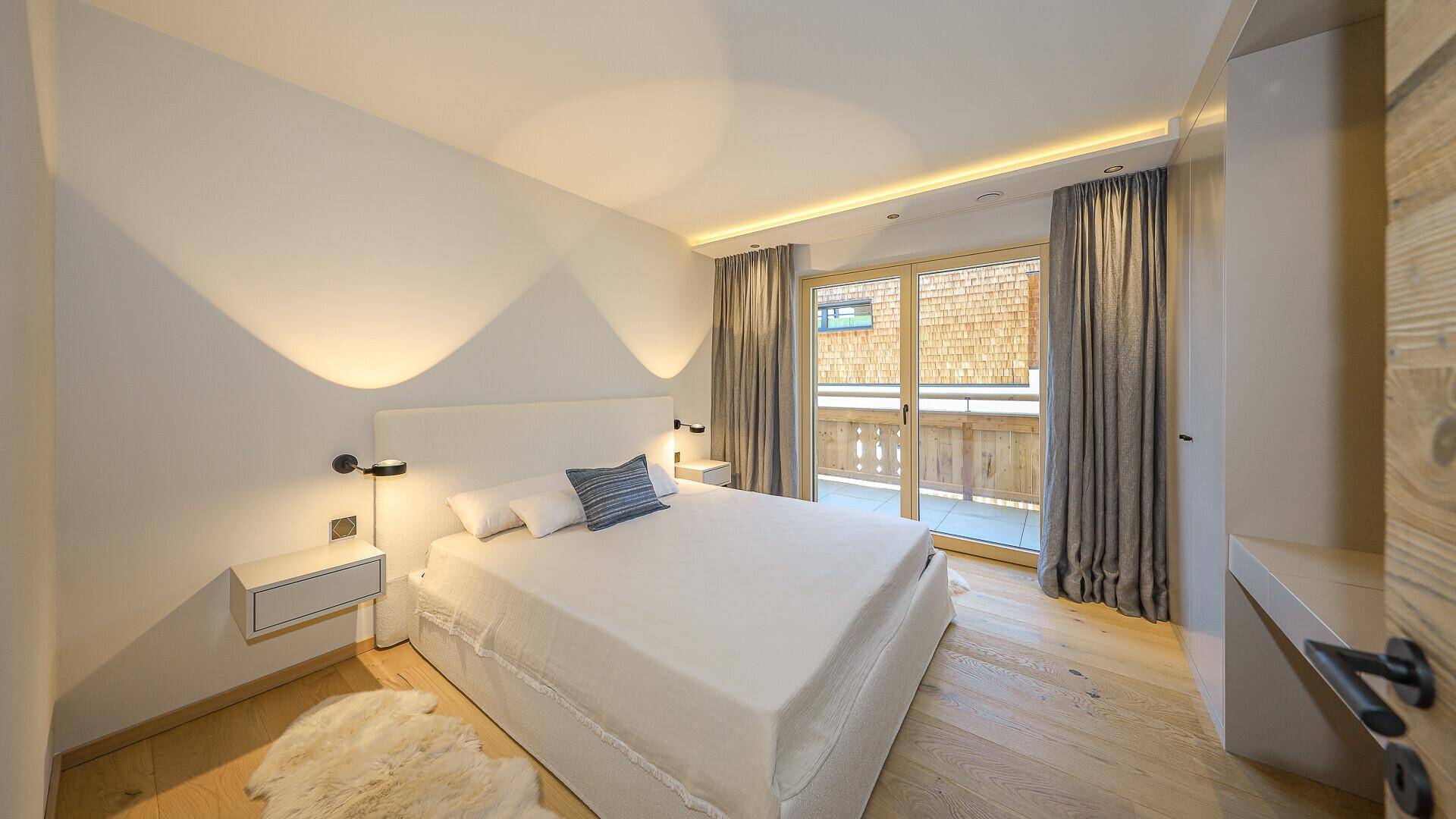 Helles Schlafzimmer mit Doppelbett, Holzboden und Zugang zu einem Balkon.