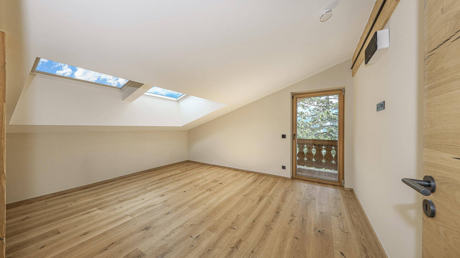 Helles Zimmer im Dachgeschoss mit Holzboden, Dachfenstern und Zugang zu einem französischen Balkon.