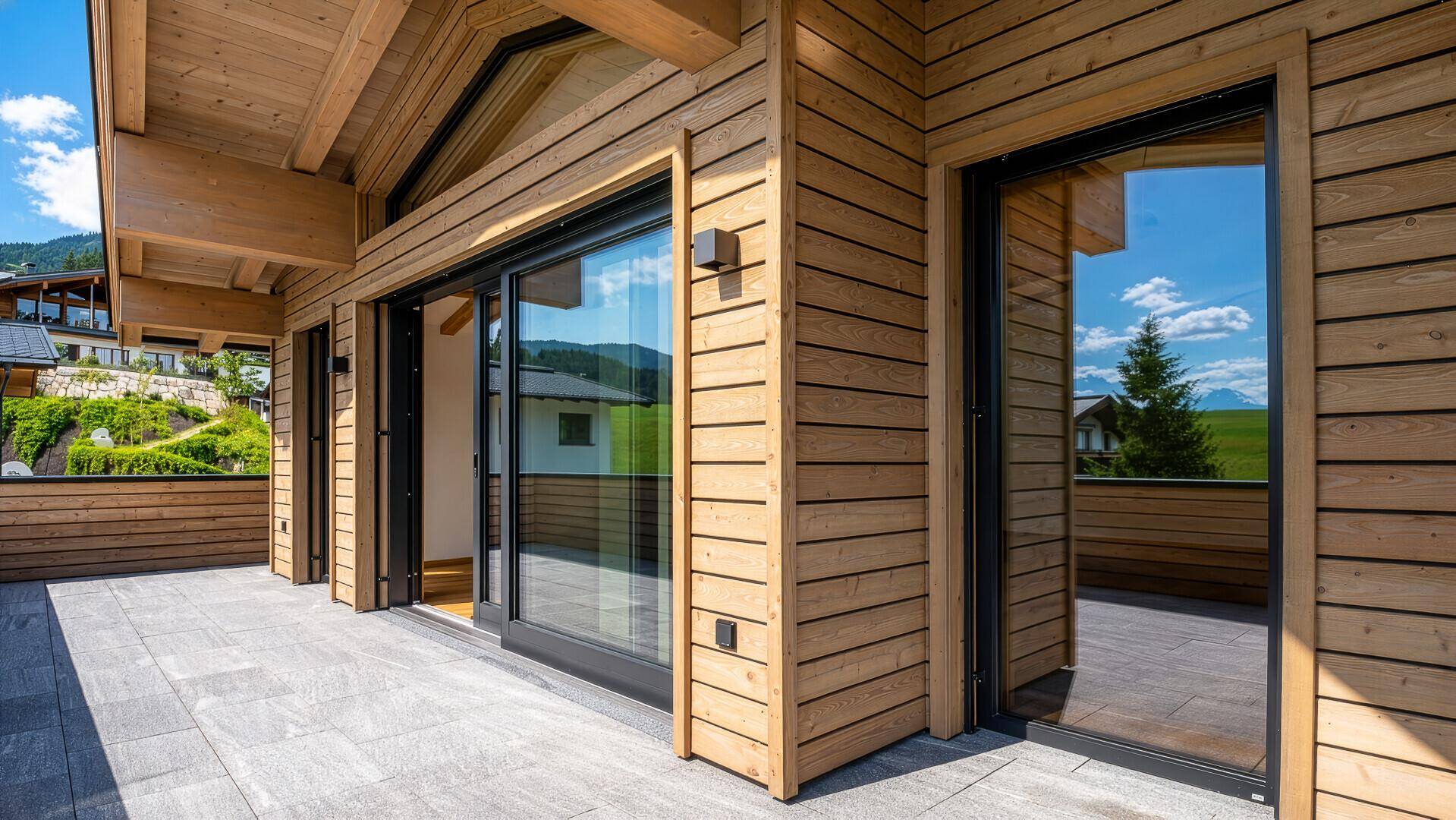 Moderne Holzfassade mit großen Schiebetüren, die auf eine geräumige Terrasse führen.