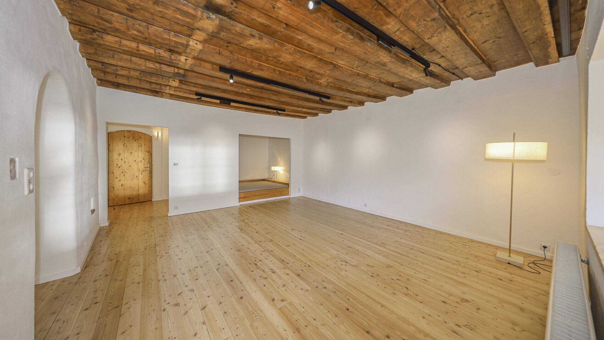 Heller Wohnbereich mit rustikaler Holzbalkendecke, Dielenboden und einer modernen Stehlampe.