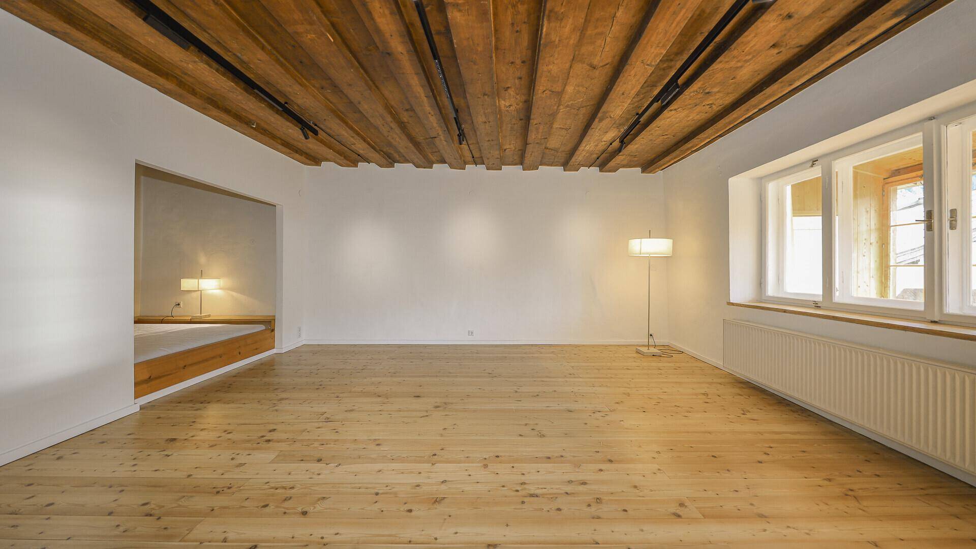 Heller Wohnraum mit Holzbalkendecke, Dielenboden, großen Fenstern und einer gemütlichen Leseecke.