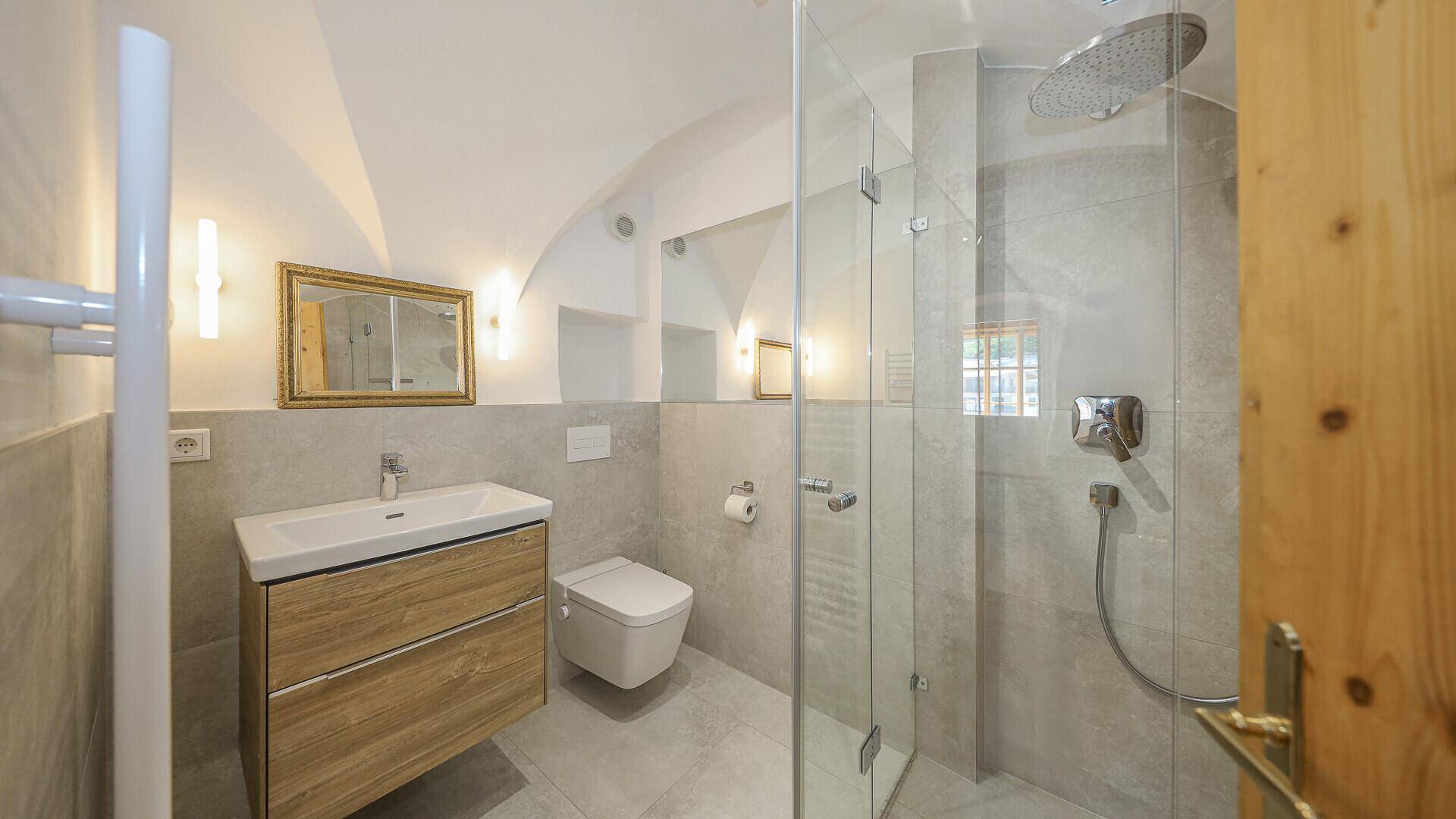 Modernes Badezimmer mit begehbarer Dusche, wandhängendem WC und stilvollem Waschtisch mit Holzunterschrank.