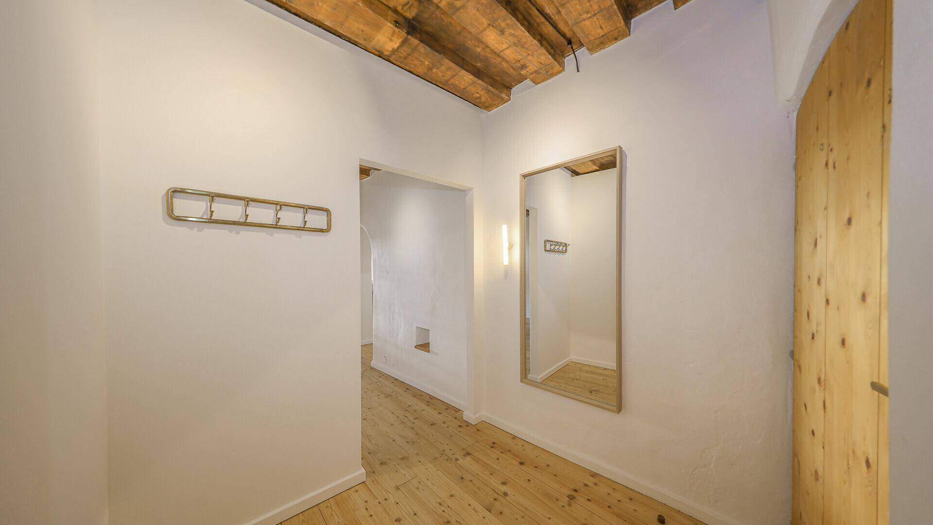 Heller Flur mit Dielenboden, Garderobe und einem großen Spiegel, der den Raum erweitert.