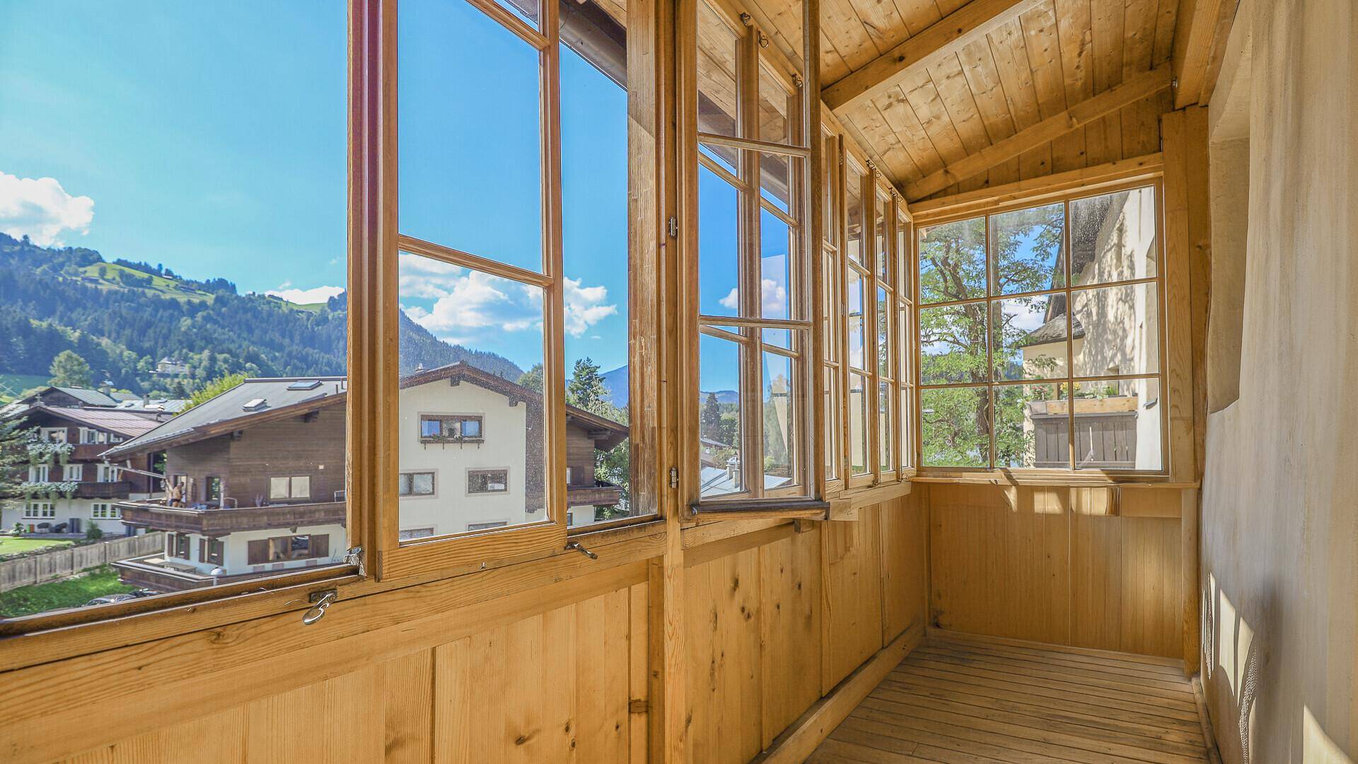Helle verglaste Loggia mit Holzboden und weitem Blick auf die umliegende Berglandschaft.