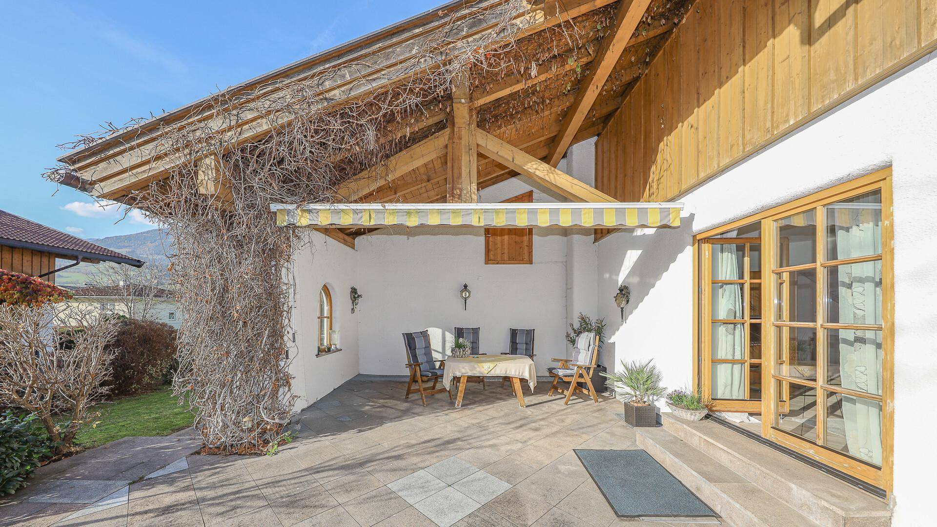 Überdachte Terrasse mit Sitzgelegenheiten, Markise und traditionellen Holzelementen.