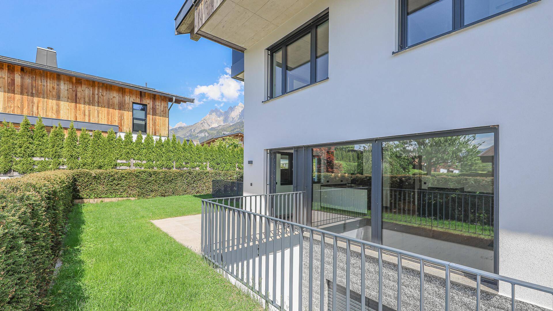 Gepflegter Gartenbereich mit Rasenfläche und Terrasse, umgeben von Hecken.