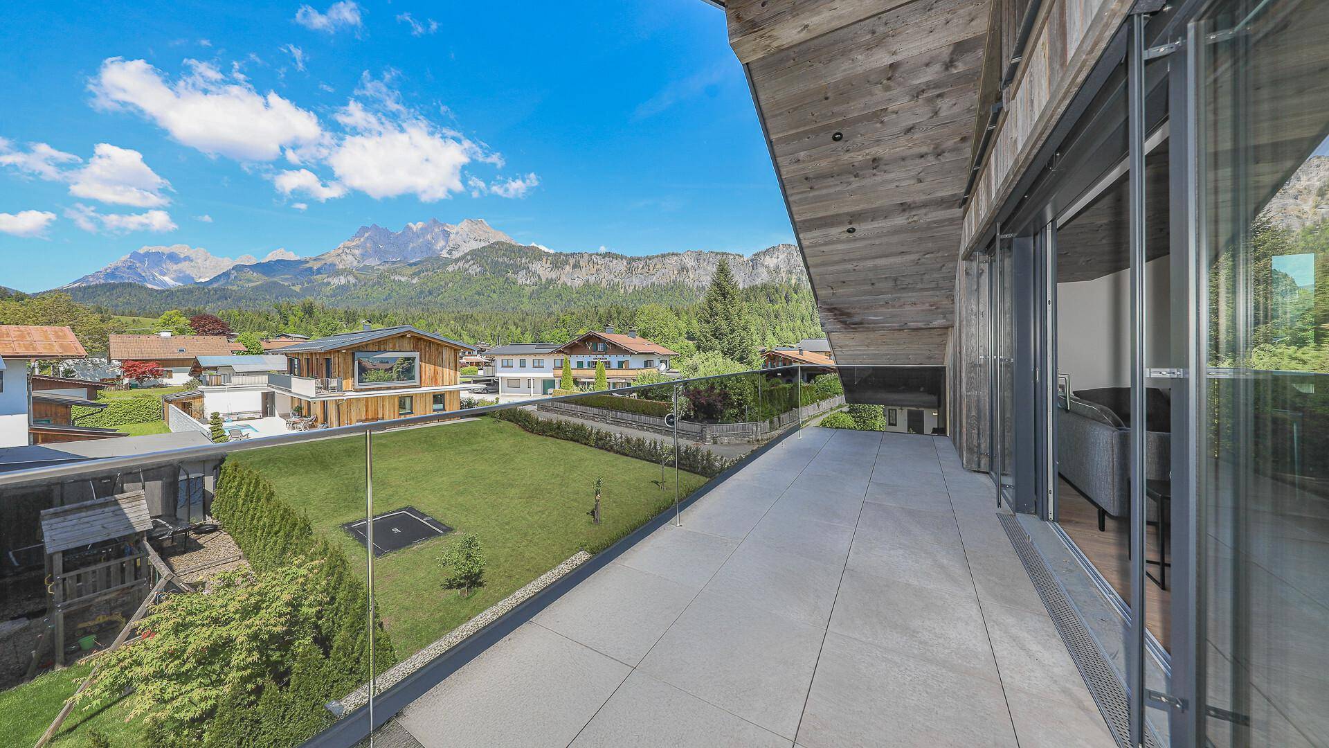 Große Terrasse mit Glasgeländer und Blick auf den Garten und die Berge.