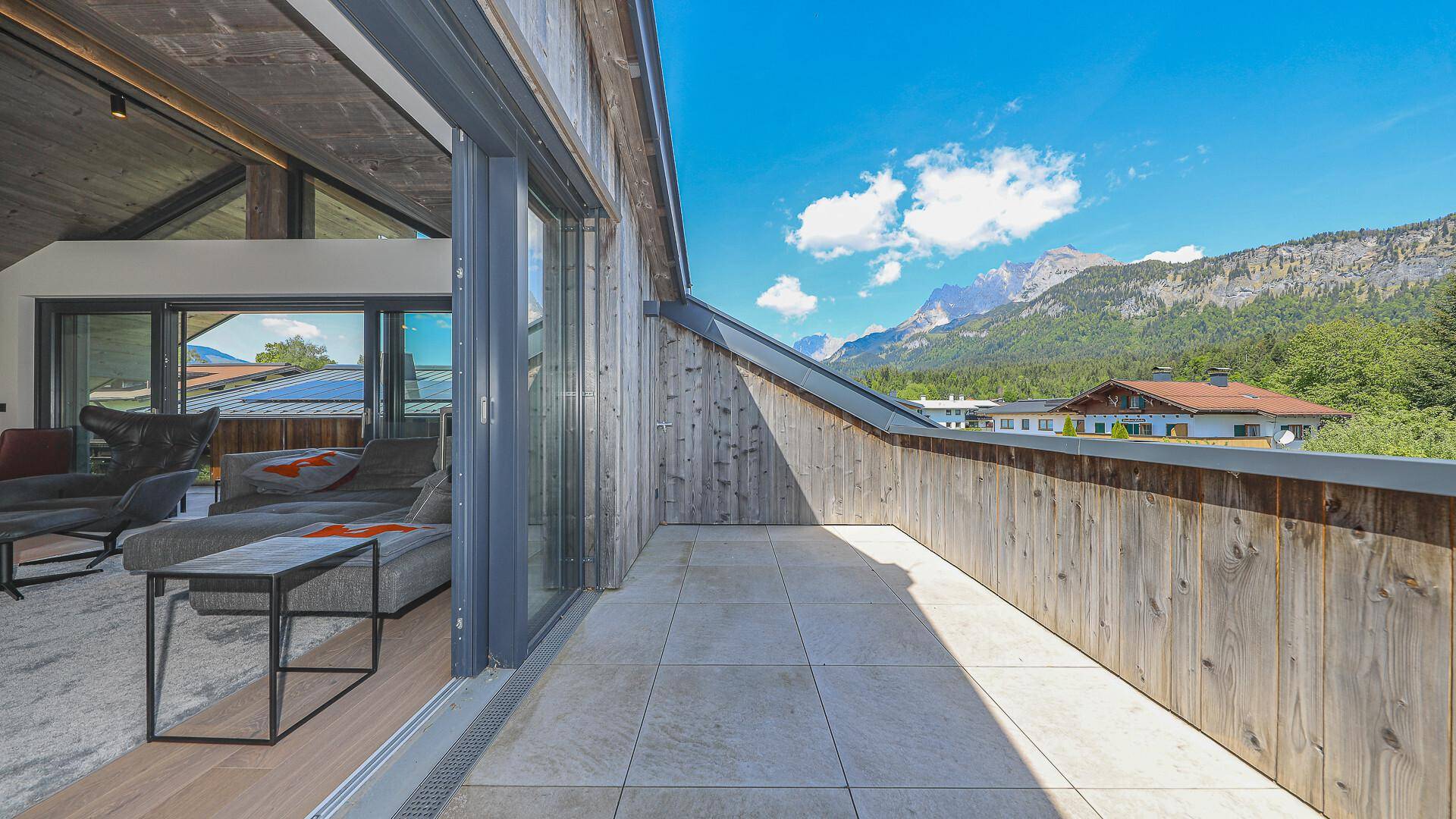 Sonniger Terrassenbereich mit Holzwänden und Zugang zum Wohnzimmer.