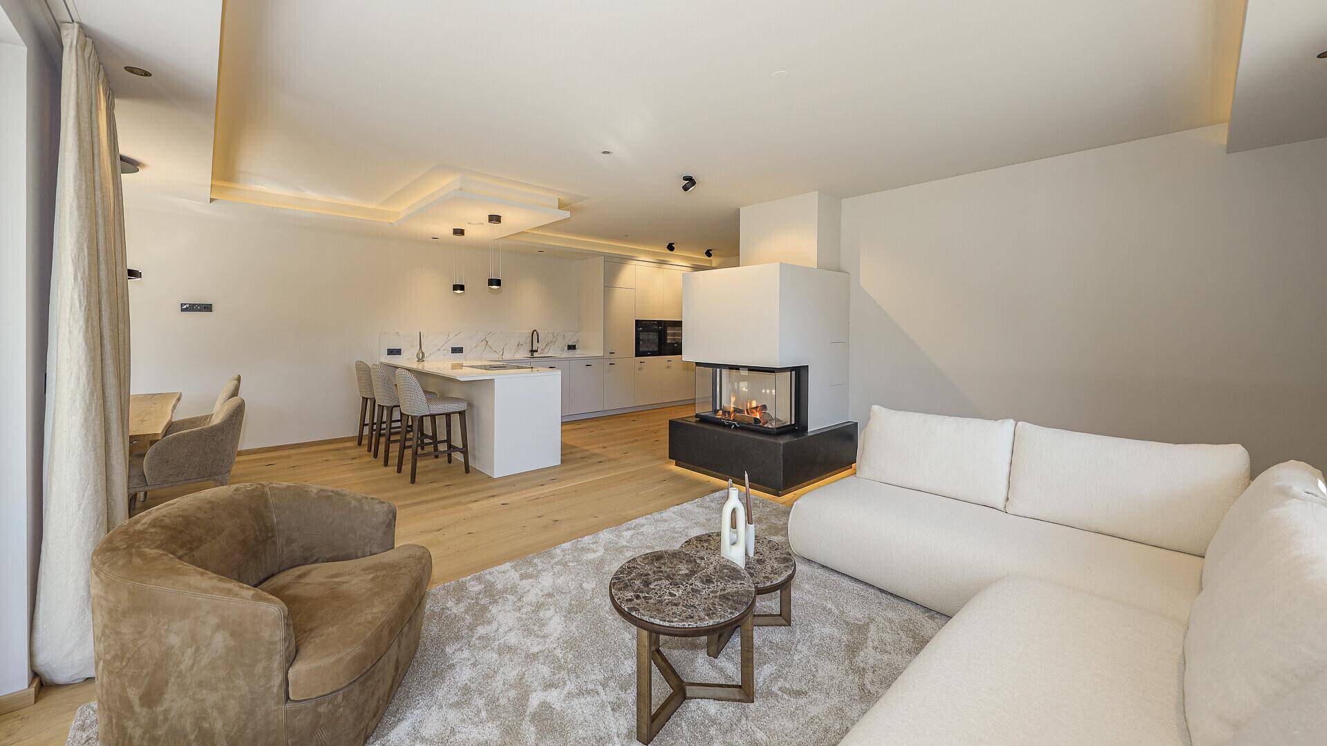 Offener Wohnbereich mit integrierter Küche, Kamin und Essbereich, ideal für geselliges Beisammensein.