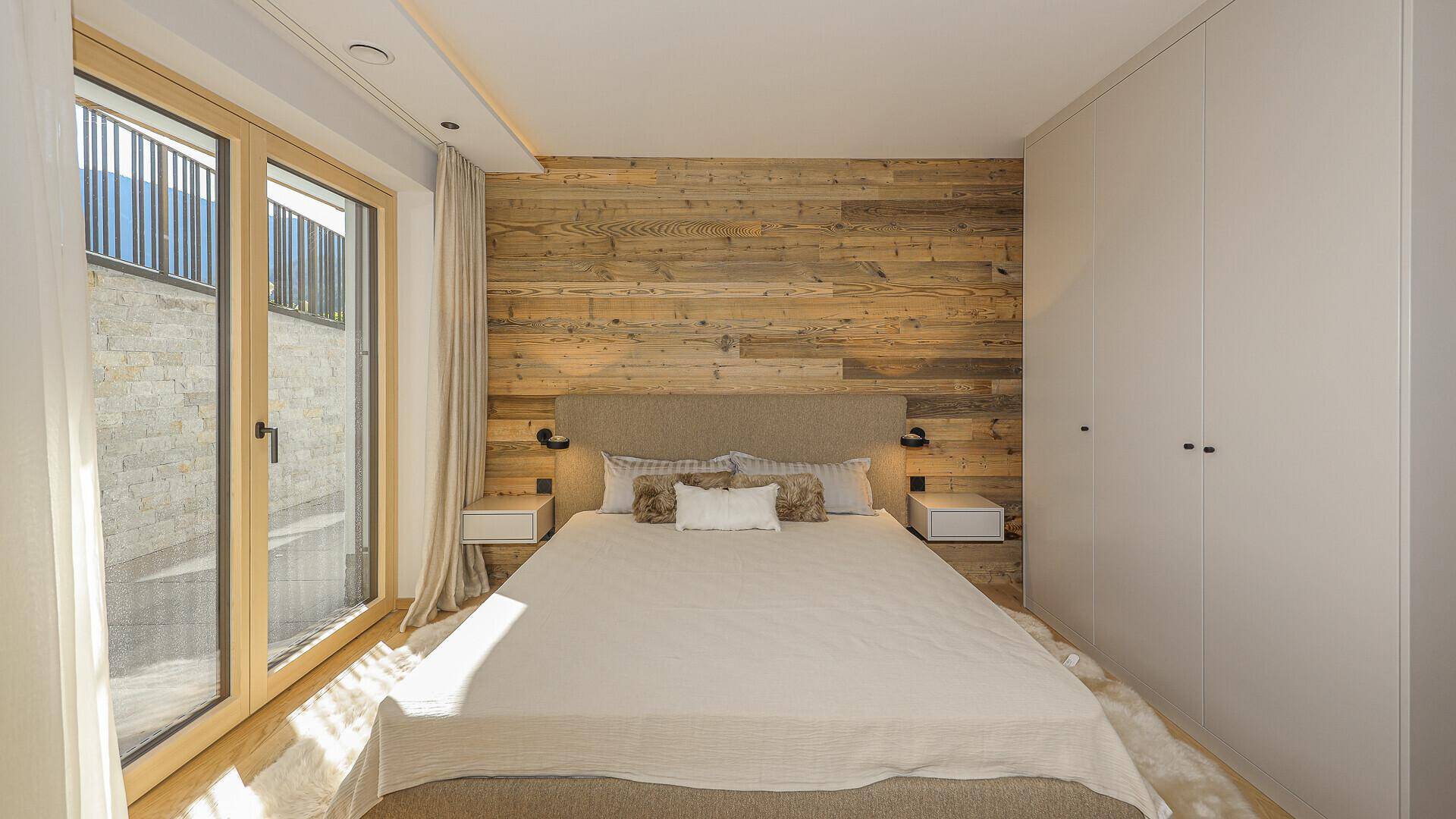Helles Schlafzimmer mit Holzwand, großem Bett und Zugang zu einem privaten Außenbereich.
