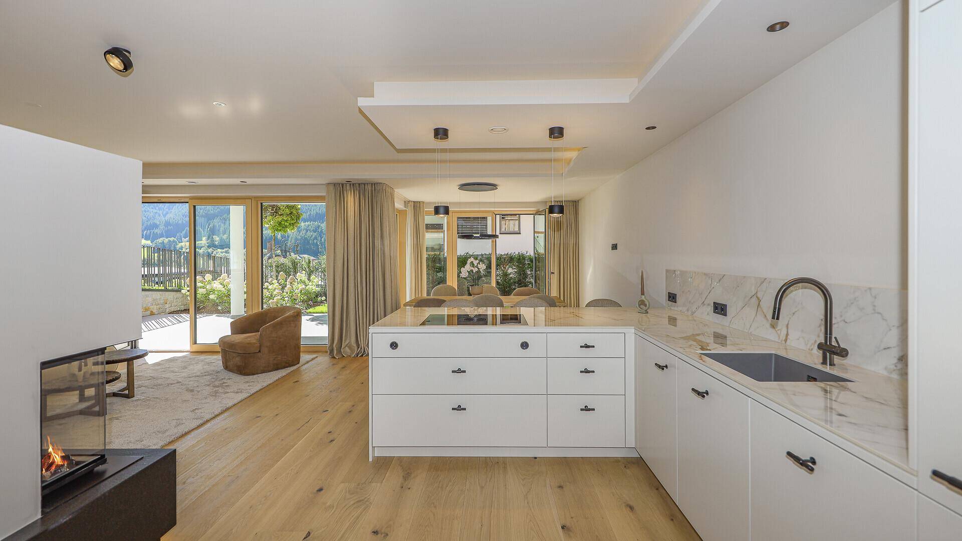 Moderne offene Küche mit Kochinsel, hochwertigen Geräten und Blick auf den Wohnbereich mit Kamin.
