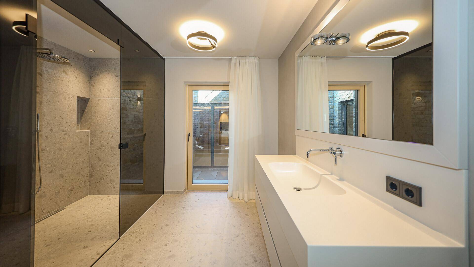 Elegantes Badezimmer mit großer Dusche, Einzelwaschbecken und Zugang zu einem Außenbereich.