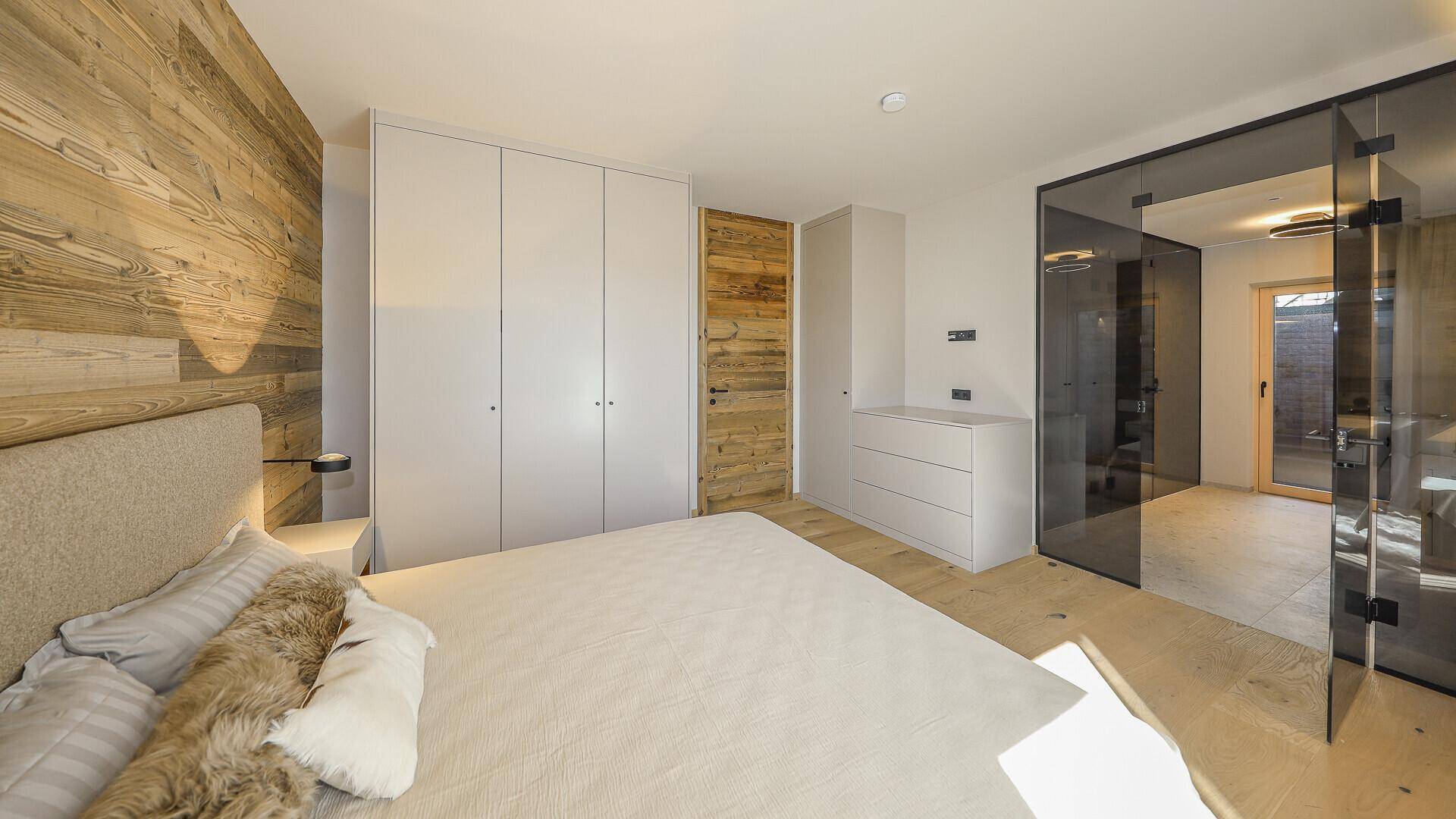 Modernes Schlafzimmer mit Holzwand, Einbauschränken und Zugang zu einem angrenzenden Bad.