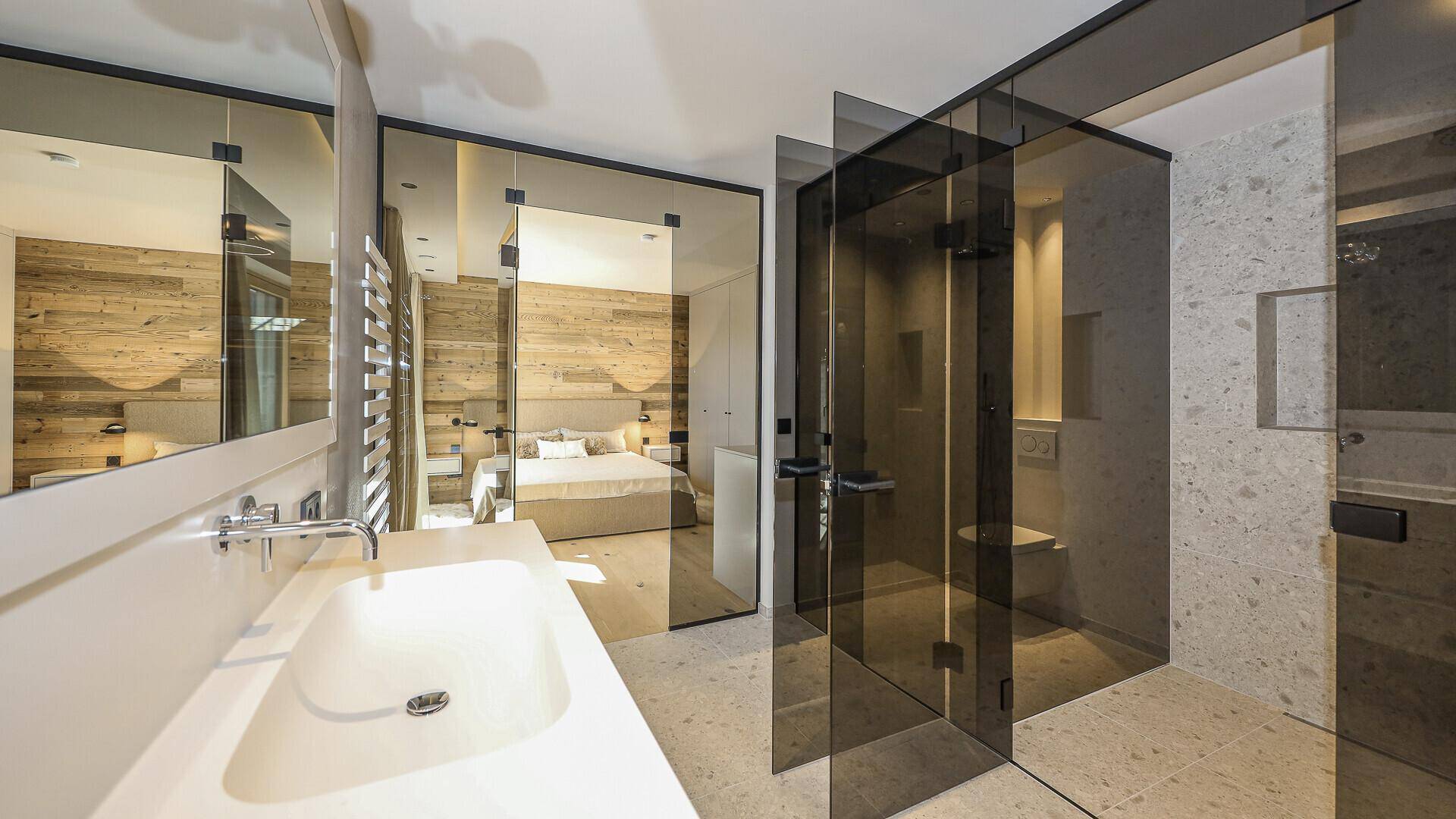 Modernes Badezimmer mit Einzelwaschbecken, begehbarer Dusche und Blick ins Schlafzimmer.