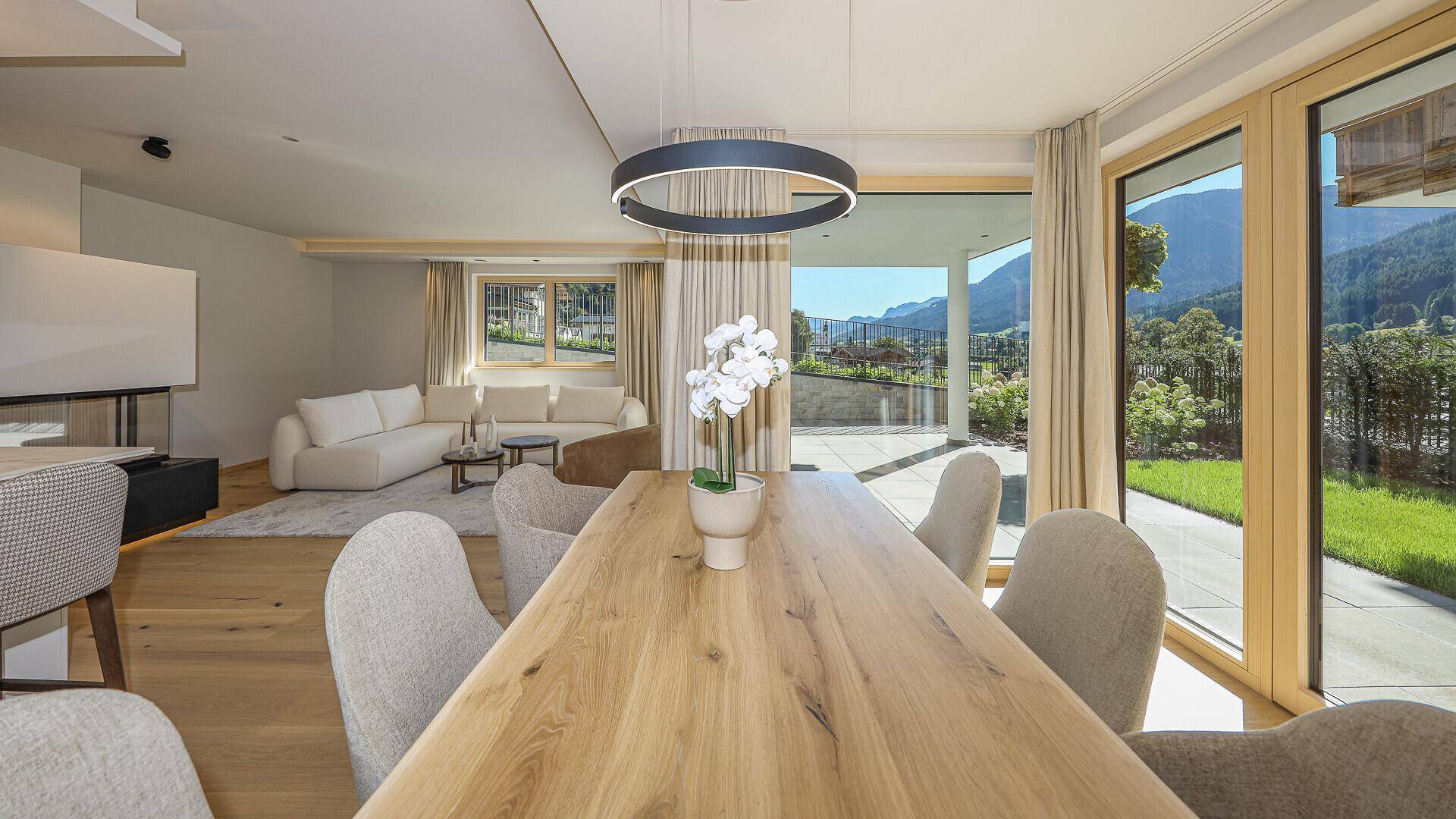 Heller Essbereich mit großem Holztisch, moderner Beleuchtung und Zugang zur Terrasse mit Bergblick.