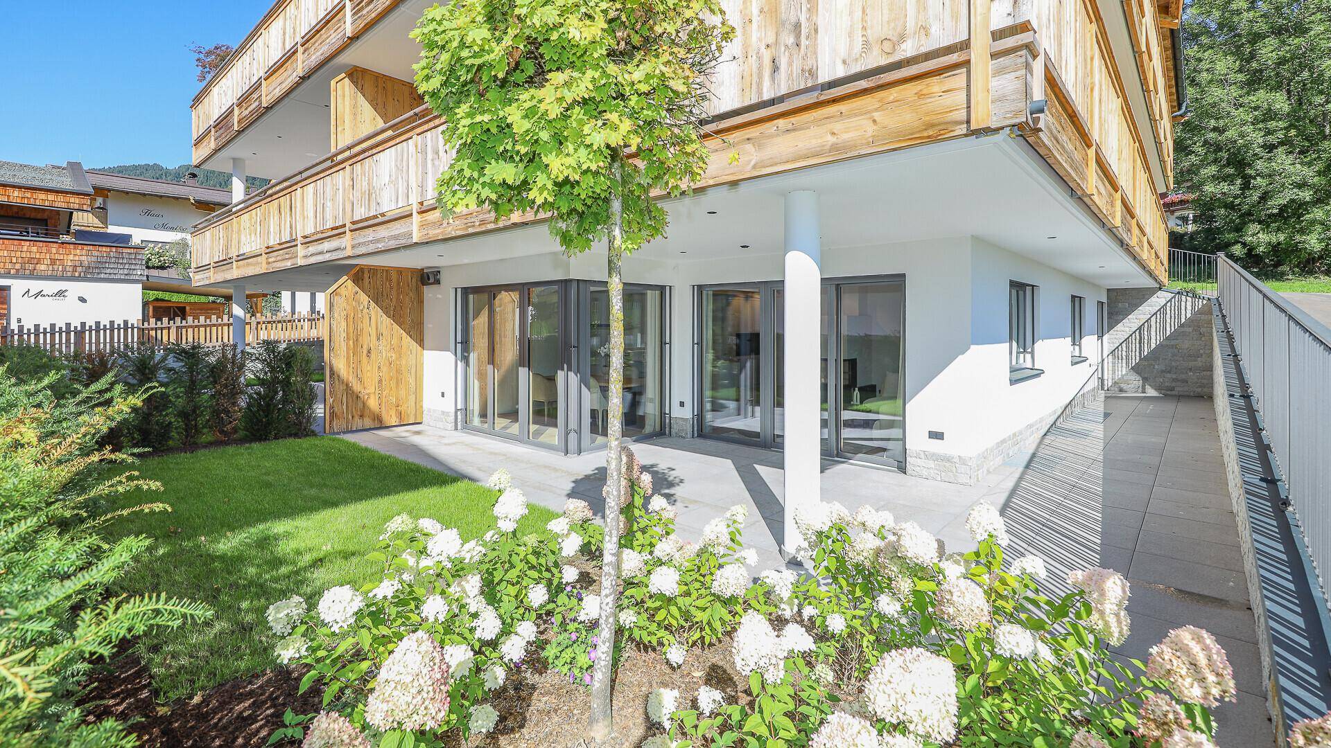 Gepflegter Garten mit blühenden Pflanzen, Terrasse und Zugang zum modernen Gebäude.