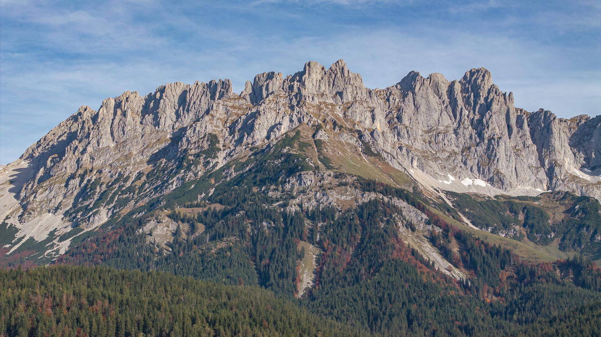 Beeindruckende Berglandschaft mit felsigen Gipfeln und dichten Wäldern in herbstlicher Färbung.