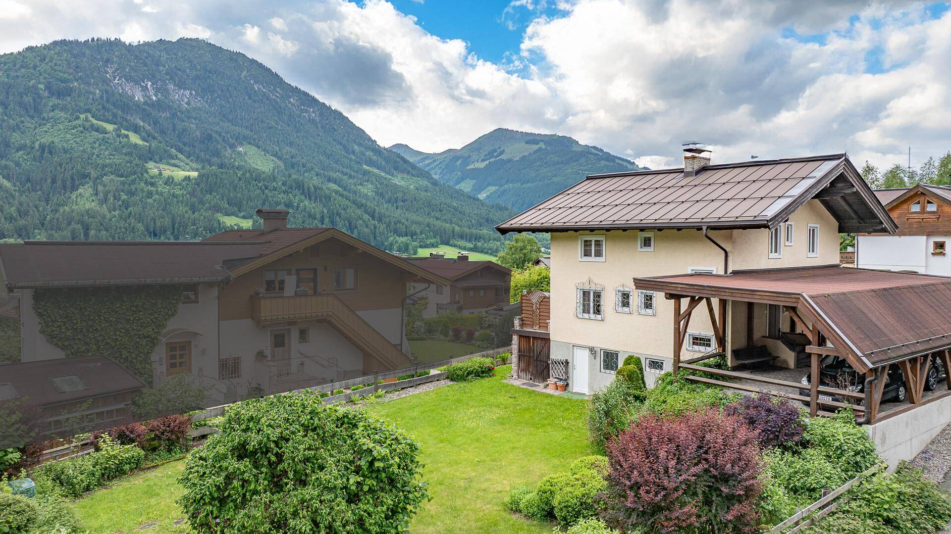 Großer grüner Garten hinter einem Haus mit überdachtem Freisitz und Blick auf die Berge.