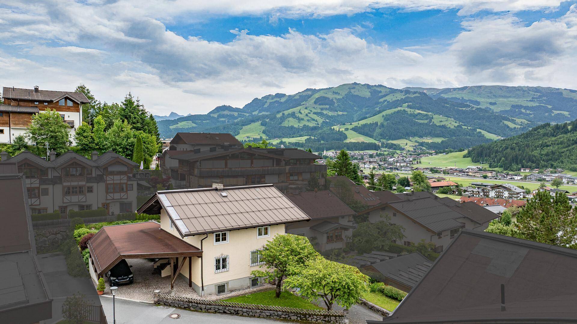 Luftaufnahme eines Hauses mit Carport und Blick auf die umliegende Wohnsiedlung und grüne Hügel.