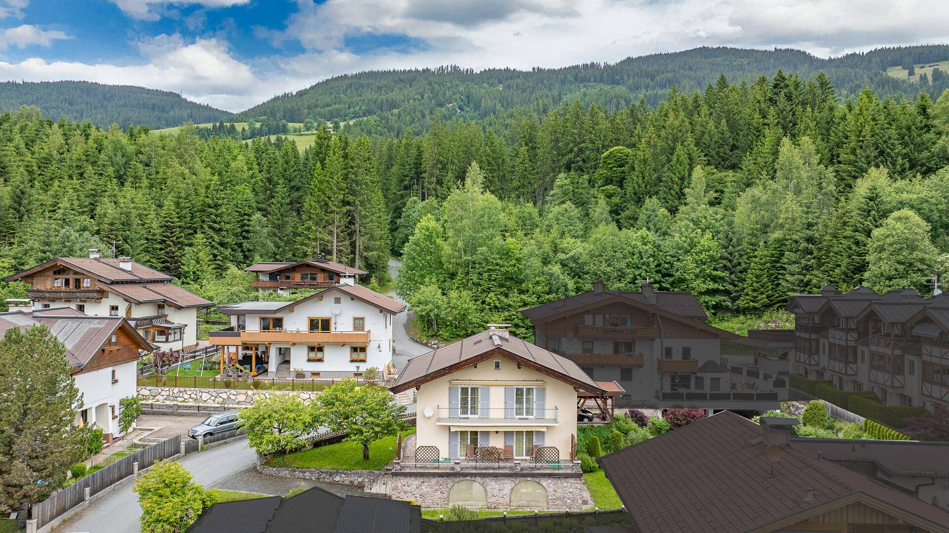 Panoramablick auf ein Wohnhaus mit Balkonen und umliegende Häuser in einer idyllischen Bergregion.